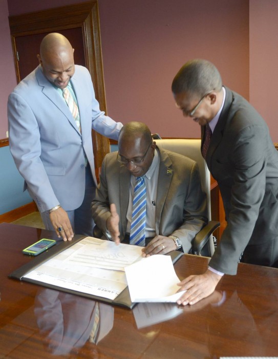 Education, Youth and Information Minister, Senator, the Hon. Ruel Reid (seated), goes over his schedule with Permanent Secretary in the Ministry, Dr. Maurice Smith (left), when he arrived for his first working day at the Ministry, at National Heroes Circle, today (March 8). At right is State Minister in the Ministry, Senator the Hon. Floyd Green. 