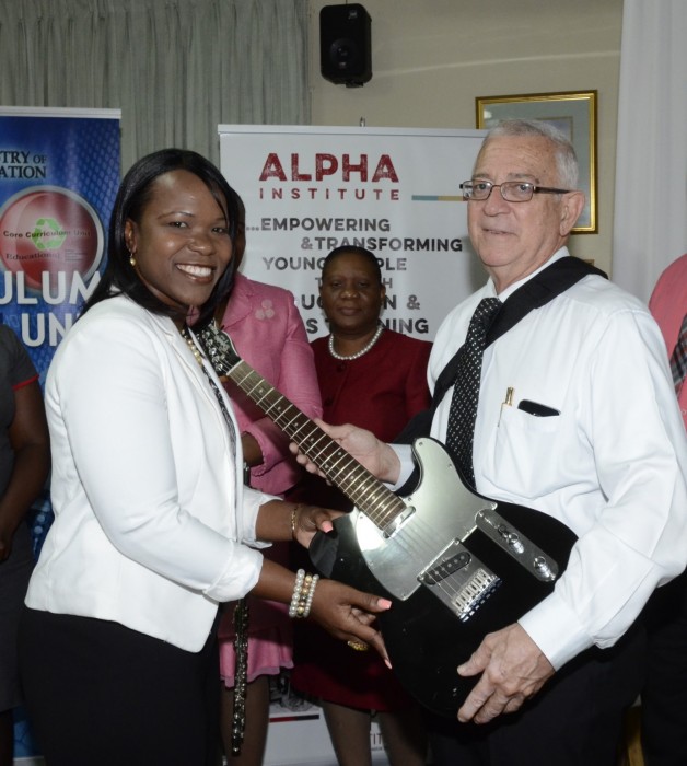 1)	Principal of Denbigh High School, Mrs. Kasan Troupe, is presented with a bass guitar by Education Minister, Hon. Rev. Ronald Thwaites, at the launch of the Music in Schools Programme and handing over of instruments, at the Alpha Institute, South Camp Road, in Kingston, on September 29. 