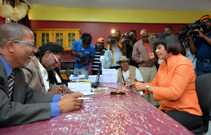 Prime Minister the Most Hon. Portia Simpson Miller (seated, right), counts her $3,000 which she is about to hand over as her nomination fee as a candidate for the constituency of South Western St. Andrew in the February 25 general election, at the Greenwich Town All Age School in Kingston, today (February 9). 