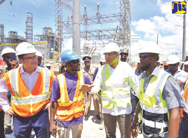 Prime Minister, the Most Hon. Holness, looks at the main generator transformer during a tour of the new US$330-million Jamaica Public Service (JPS) 190-megawatt (MW) power plant being built in Old Harbour Bay, St. Catherine. Looking on are JPS President and Chief Executive Officer, Emanuel DaRosa (left), and Senior Project Director, Timothy Lamb.