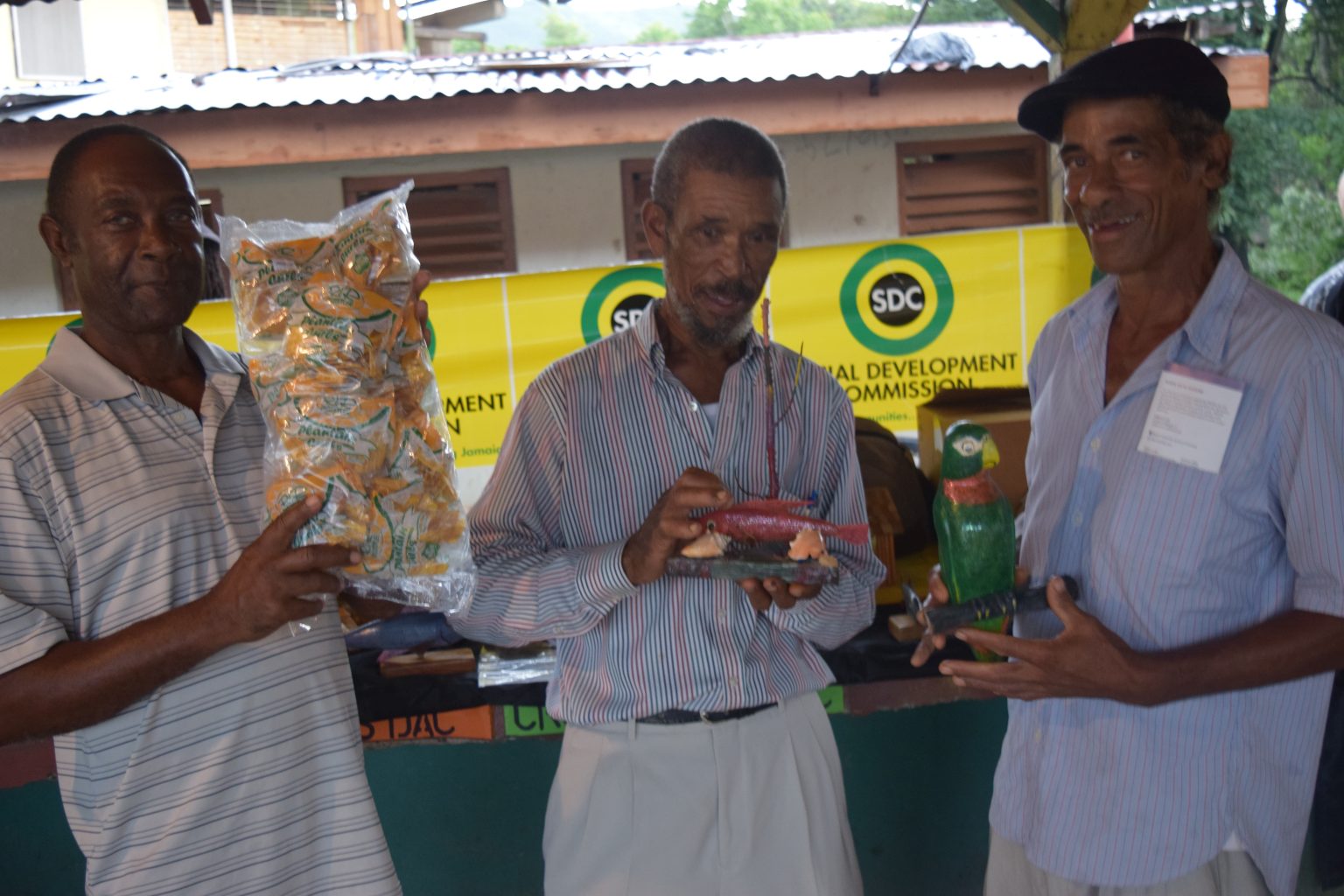 Chairman of the Cross Keys Development Area Committee, Smeadley Reid (left), displays a bag of Cross Keys DAC Plantain Curls, at a recent Social Development Commission (SDC) Business Fair. With  Mr. Reid (from second left) are Hudlyn Pitter and Neville Swaby .