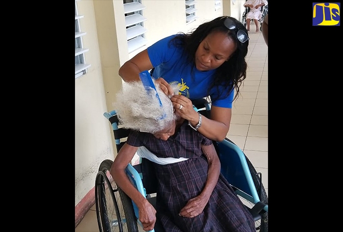 Member of the Northern Caribbean University (NCU) Behavioural Sciences Club, Rasmeha Raymond (standing), combs the hair of a resident at the St. Thomas Infirmary, during a visit to the institution by members of the group on March 1. 
