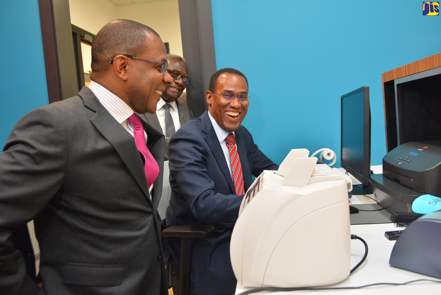 Minister of Finance and the Public Service, Dr. the Hon. Nigel Clarke (right), tries out a computer in one of the offices at the Victoria Mutual Fairview Financial Centre, following the official opening of the facility in Montego Bay, St. James on April 24. Looking on are Chief Executive Officer of Victoria Mutual Group, Courtney Campbellon (left); and Custos of St. James, Conrad Pitkin.