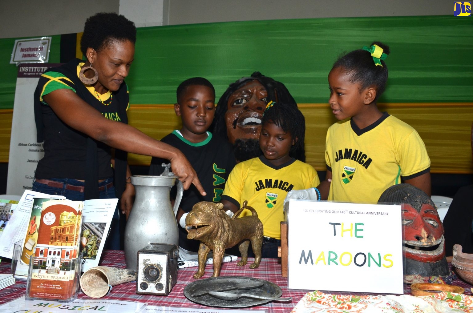 Assistant Education Officer at the Institute of Jamaica, Stephanie Rose (left), interacts with students of Jessie Ripoll Primary School, Camp Road, Kingston, at an exhibition held on Jamaica Day (February 22) at the National Arena in Kingston. 