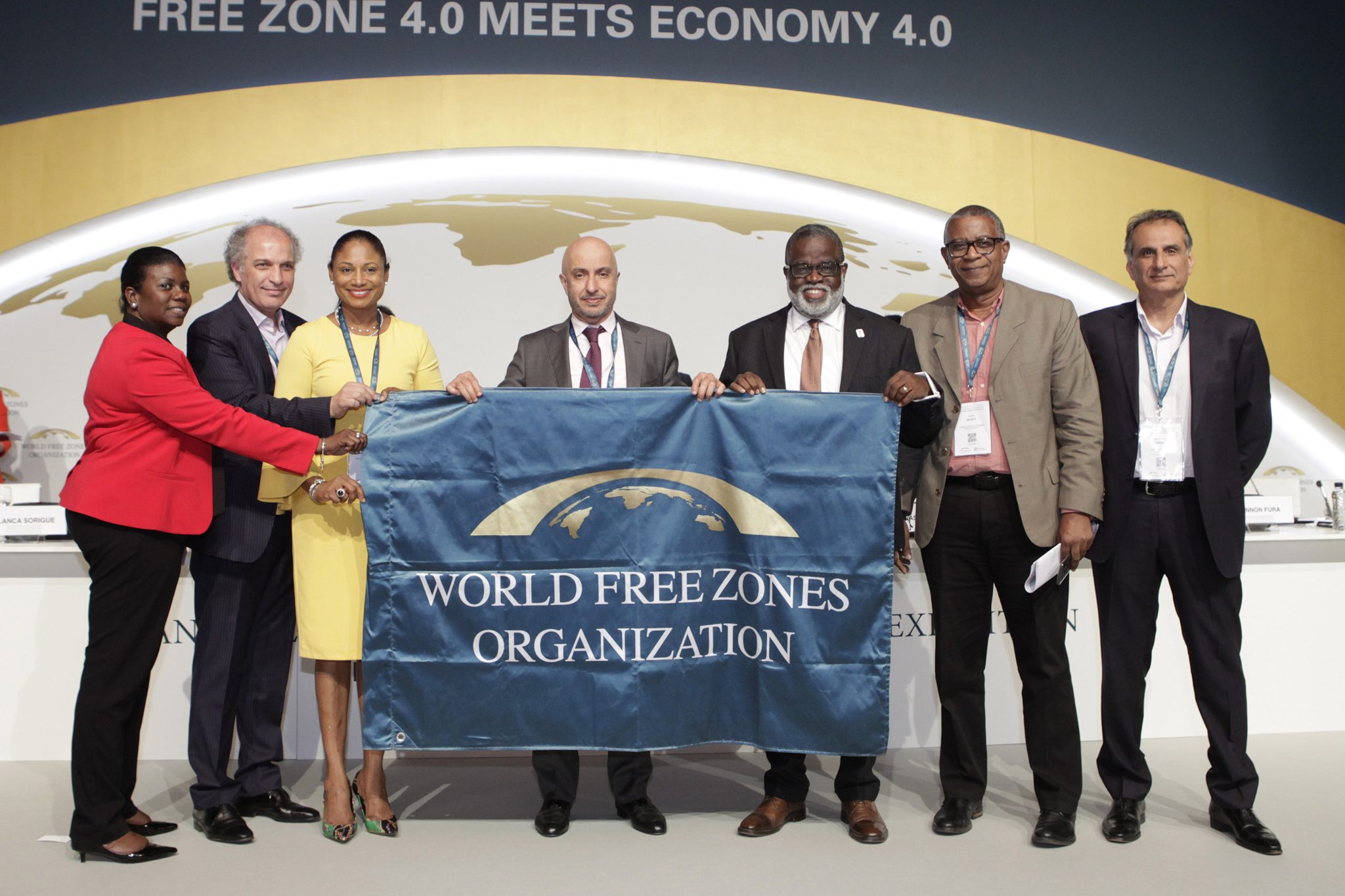 Chief Executive Officer of the Jamaica Special Economic Zones Authority (JSEZA), Dr. Eric Deans (third right), joins in displaying the WFZO banner at the organisation's 2019 conference held in Barcelona, Spain, in June.  This follows the announcement of Jamaica winning the bid to host the conference in 2021.  From left are Senior Director, Technical Services and Infrastructure Development, JSEZA, Sanvia Martin-Bailey; Chief Executive Officer (CEO), WFZO, Dr Samir Hamrouni; Regional Director, Jamaica Tourist Board, Odette Soberam Dyer; Chairperson, Board of Directors, WFZO, Dr Mohammed Alzarooni; Chief Operating Officer, JSEZA, Gary Scott; and Director, Operations, WFZO, Suresh Poduval.