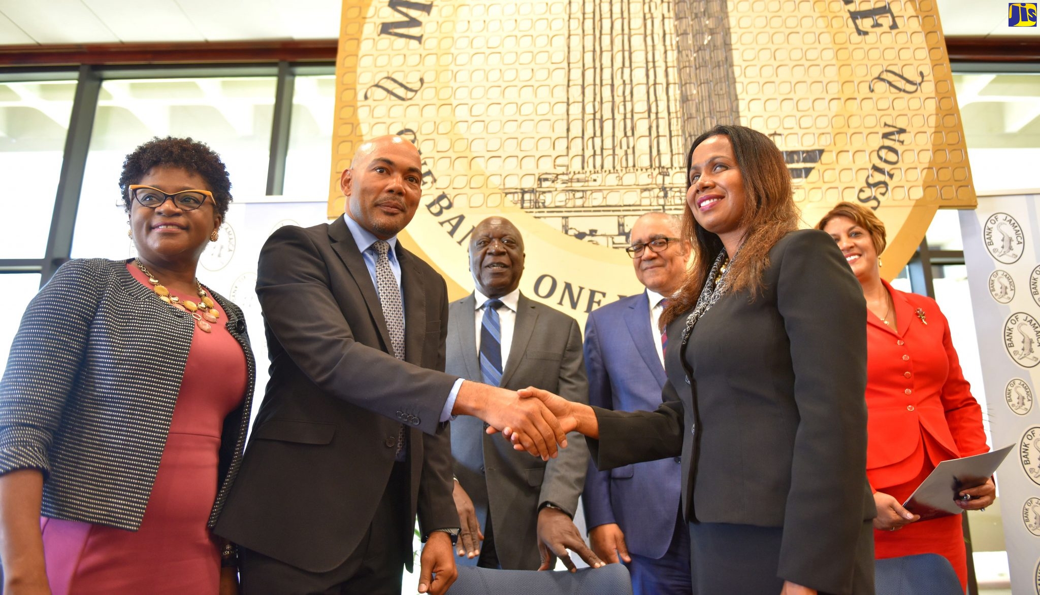Bank of Jamaica (BOJ) Governor, Brian Wynter (second right, background), observes as Jamaica Bankers Association (JBA) President, Jerome Smalling (second left), and Cambio Association of Jamaica (CAJ) President, Heather Ferguson Fearon (right, foreground), shake hands after signing the Bank for International Settlements (BIS) Foreign Exchange (FX) Global Code at the BOJ in downtown Kingston on Monday (July 29). Looking on (from left) are Jamaica Institute of Financial Services (JIFS) Executive Director, Darlene Jones; and BOJ Deputy Governors, John Robinson and Natalie Haynes.