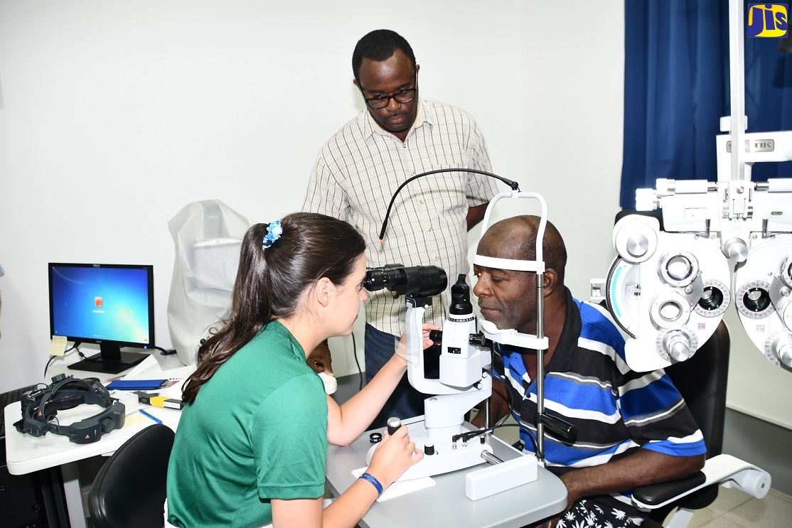 President of the Lions Club of Montego Bay, O'Neil Daley (centre), observes  as Stephanie Schumacher (left) from the Volunteer Optometric Services to Humanity (VOSH) performs an eye examination on Hubert Cummings. Occasion was a medical mission by ophthalmologists from Canada Vision Care (CVC) and the United States-based Hawaiian Eye Foundation at the Community Vision Centre of Excellence on Albion Road, St. James, last month.