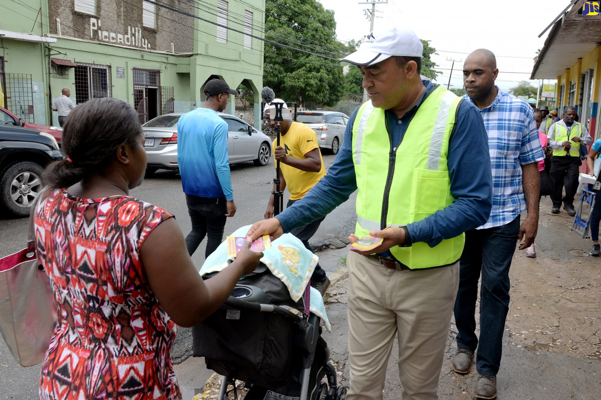 Minister of Health and Wellness, Dr. the Hon. Christopher Tufton (second left), distributes brochures on the dengue virus to a passerby in Spanish Town, St. Catherine, yesterday (September 26) while on a tour of the town. In an effort to eradicate the Aedes aegypti mosquitoes that cause dengue, the Ministry, through the National Health Fund (NHF), has earmarked more than $130 million and more than 1,000 temporary vector workers to search and destroy mosquito breeding sites across the island as well as to boost public education on the disease.