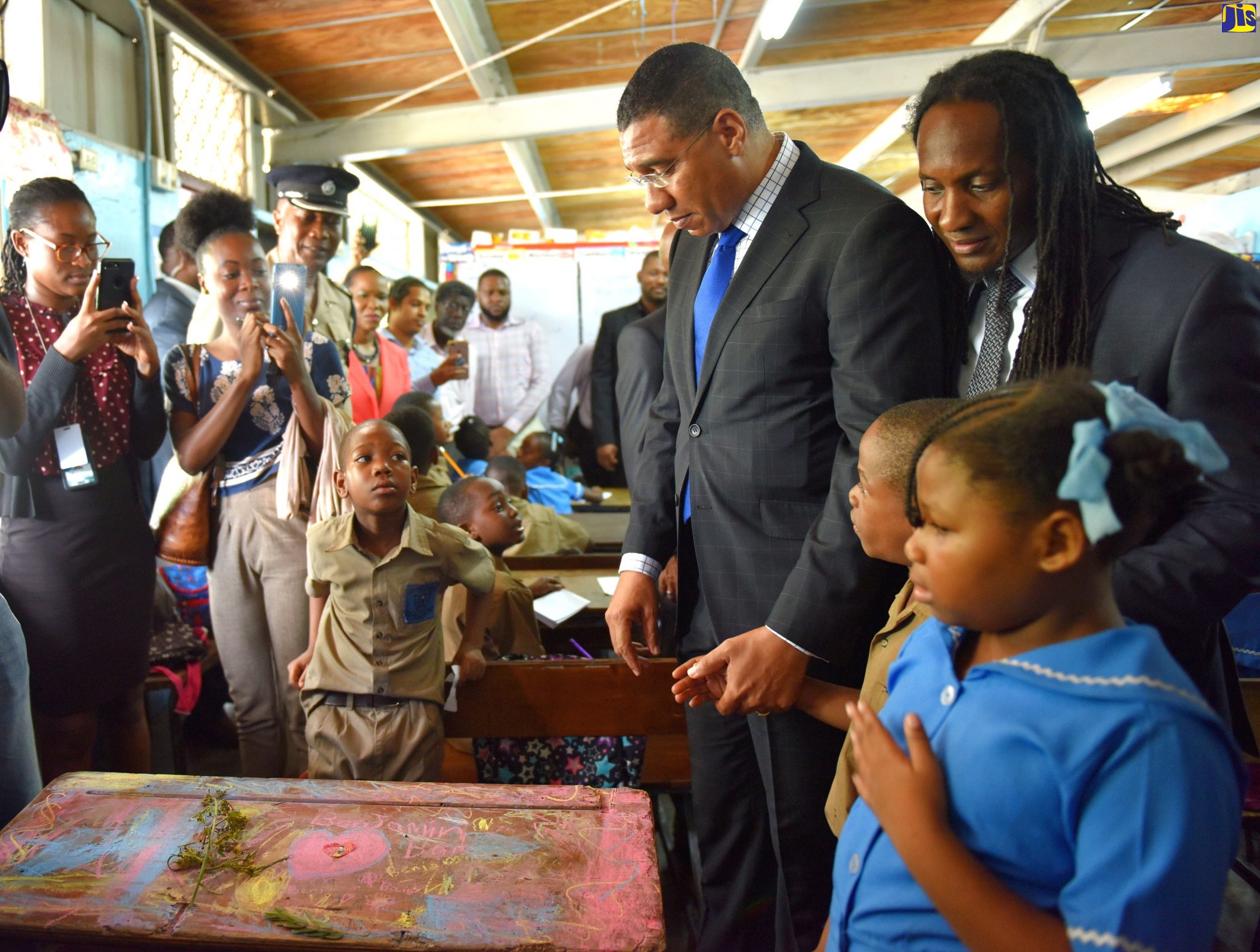 Prime Minister, the Most Hon. Andrew Holness (second right, background), holds the hand of Clan Carthy Primary School student, Naquan Smith (second right, foreground), while looking at the desk formerly occupied by his late classmate, Benjamin Bair, who died tragically at the institution, located on Deanery Road in Kingston, on Monday (October 28). Among those also looking on are State Minister in the Ministry of Education, Youth and Information, Hon. Alando Terrelonge (background right), and student, Damoya Wright (right).