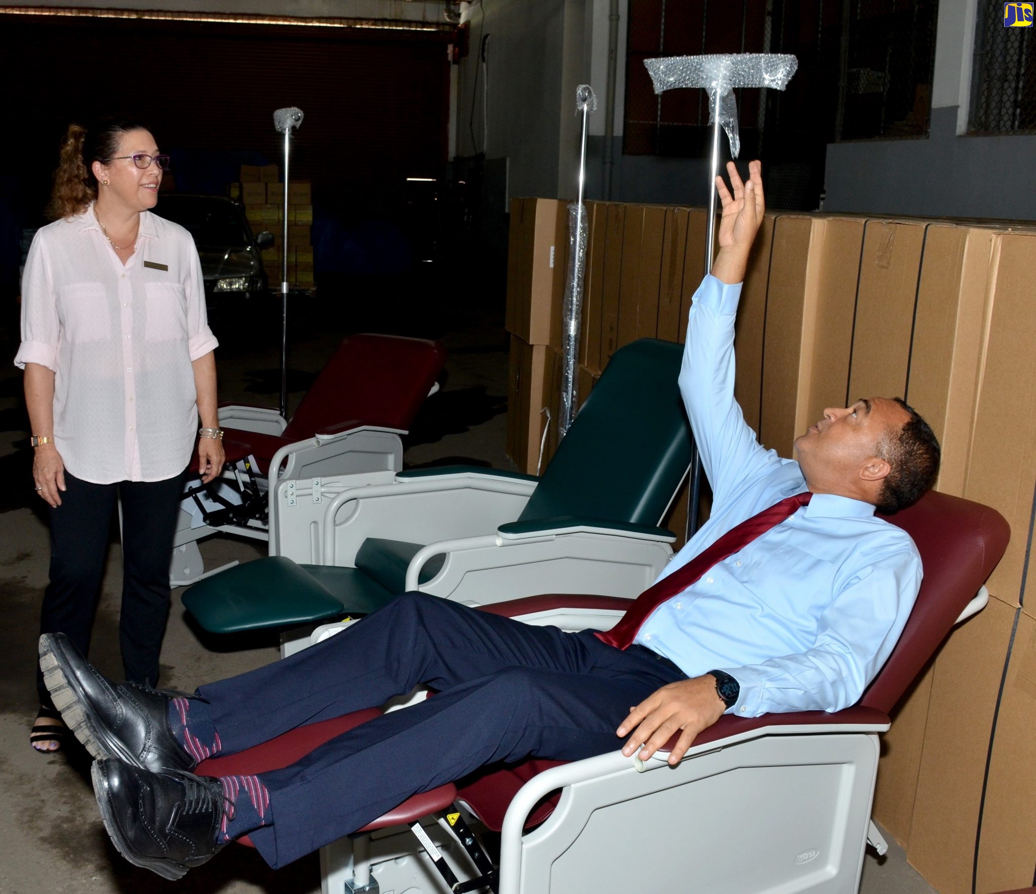 Minister of Health and Wellness, Dr. the Hon. Christopher Tufton (right), tests one of the new hospital reclining chairs that will soon be distributed to hospitals across the island, on Tuesday (October 22) at the Ministry’s warehouse, in Kingston. At left is Senior Medical Representative, Jamaica Hospital Supplies, Tanya March.