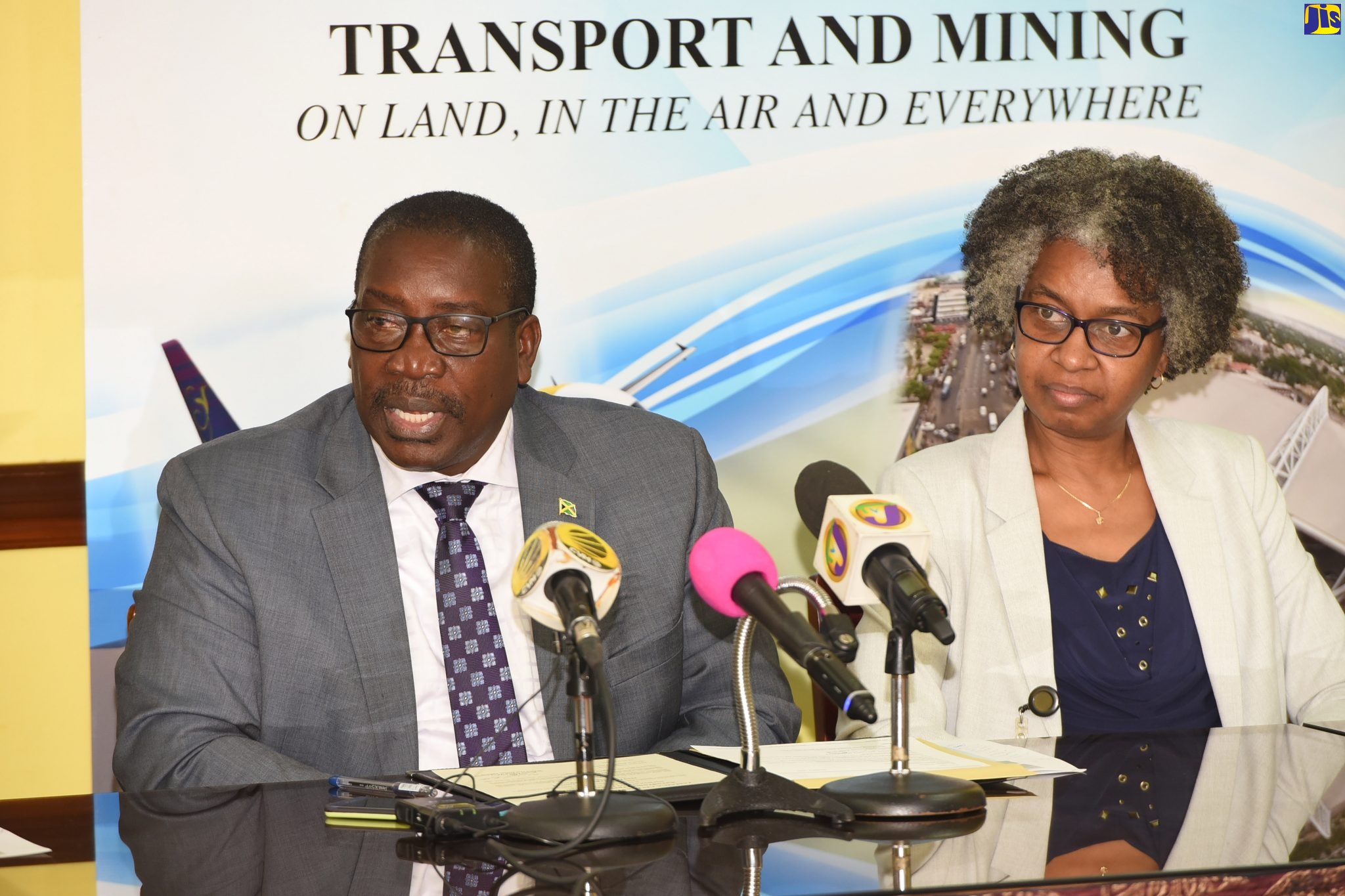 Minister of Transport and Mining, Hon. Robert Montague, speaking at a cremony for the presentation of an Aerodrome Operator Certificate to the Norman Manley International Airport (NMIA) at the Ministry’s office in Kingston on Tuesday (October 8).  Seated beside him is Chief Technical Director in the Ministry, Dr. Janine Dawkins.