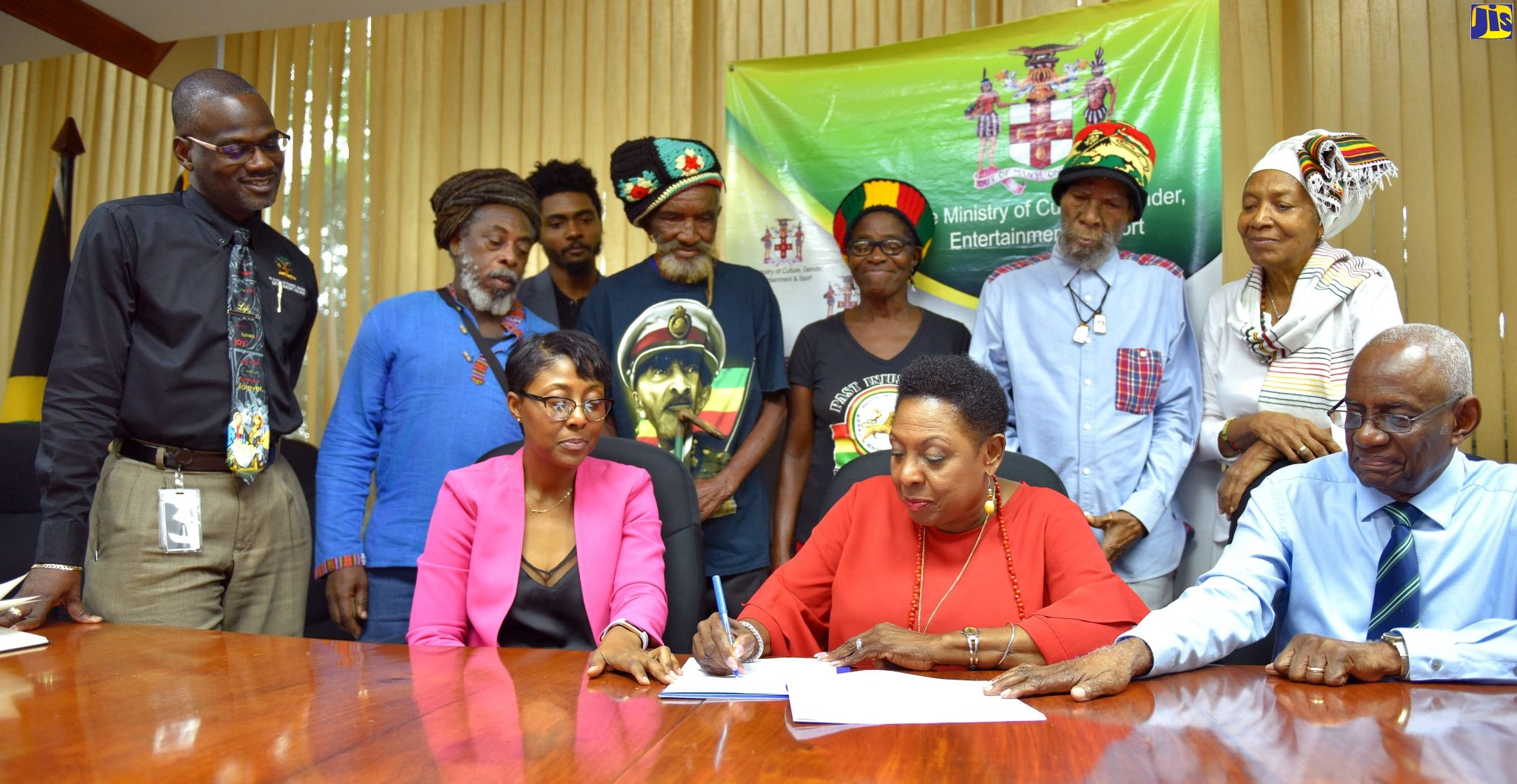 Minister of Culture, Gender, Entertainment and Sport, Hon. Olivia Grange (seated, centre),  signs Deed for the Coral Gardens Trust Fund, at the Ministry, in Kingston,  on Thursday (December 19). Witnessing the moment are: Permanent Secretary, Ministry of Culture, Gender, Entertainment and Sport, Denzil Thorpe (standing, left); Legal Executive, Administrator-General’s Department, Kedia DaLattayae (seated, left); pastor Winston Malcolm; victims of the Coral Gardens incident and executives of the Rastafarian Coral Gardens Benevolent Society.