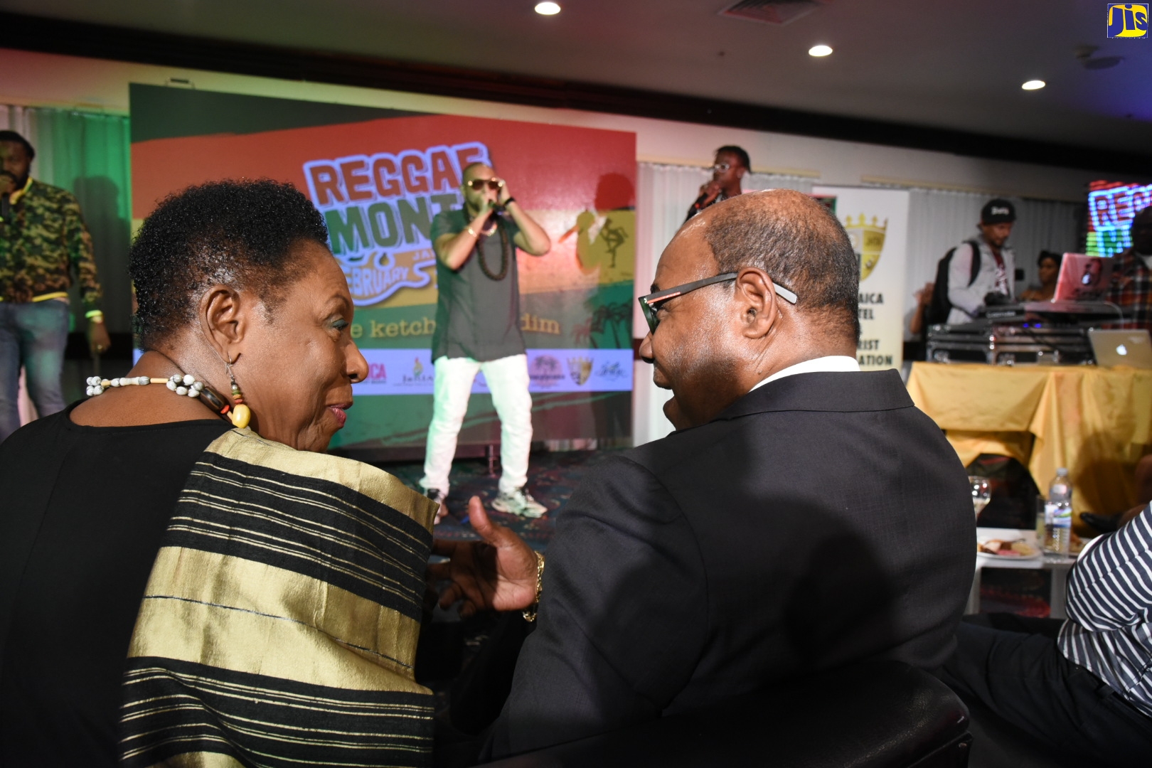 Minister of Culture, Gender, Entertainment and Sport, Hon. Olivia Grange (left), converses with Minister of Tourism, Hon. Edmund Bartlett, during Tuesday’s (December 3) media launch of activities to observe Reggae Month 2020, at The Jamaica Pegasus hotel in New Kingston. The events will be held throughout February 2020 under the theme ‘Come ketch de Riddim’. Performing in the background is Grammy-winning international dancehall artiste, Sean Paul.