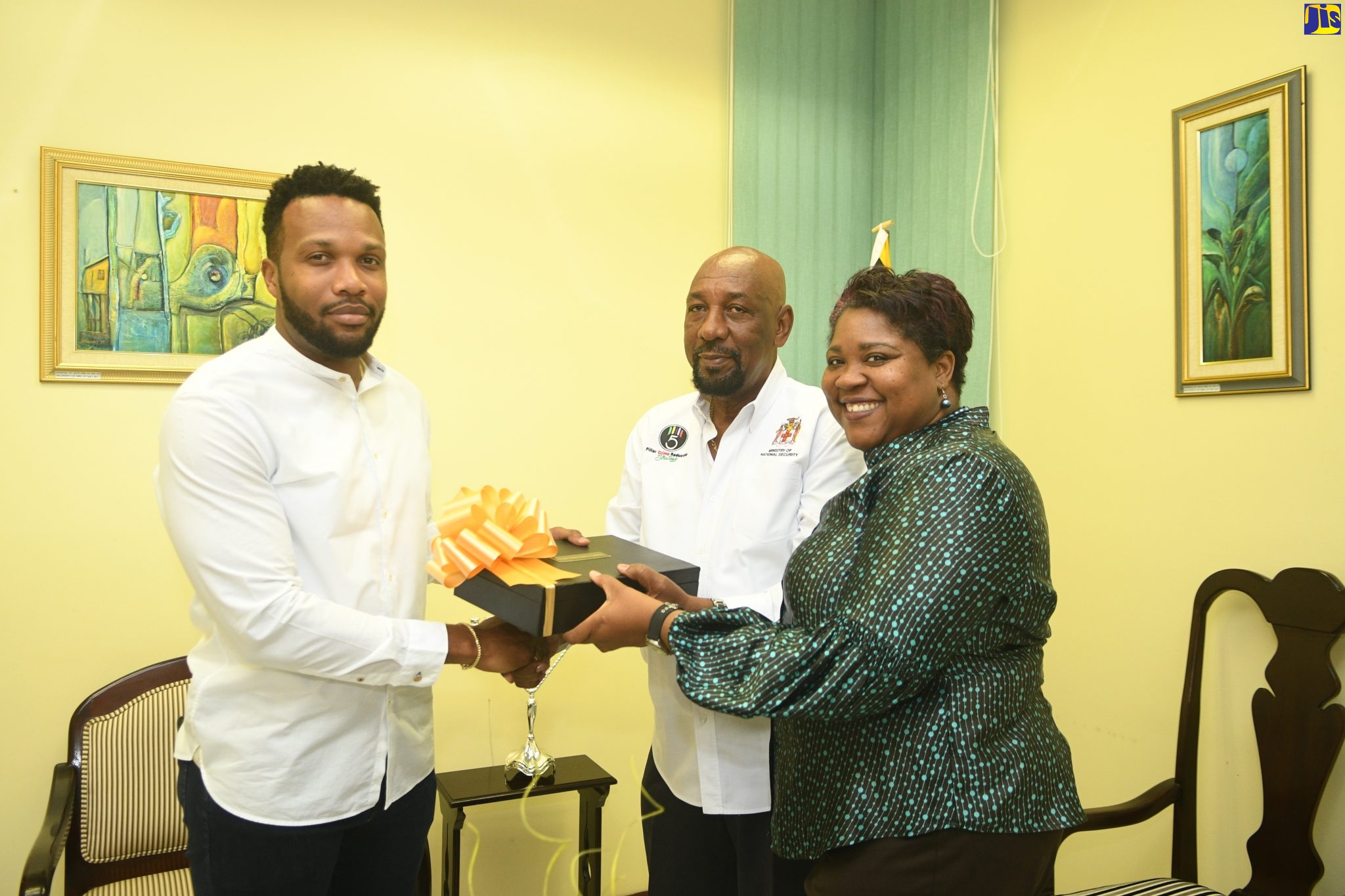 Minister of State in the Ministry of National Security,  Hon. Rudyard Spencer (centre); and Acting Chief Technical Director, Ministry of National Security, Shauna Trowers (right), present a box with a  trophy to ‘We Transform’ Ambassador and Mentor, Jeffrey “Agent Sasco” Campbell, at the Ministry in Kingston, on December 18.
