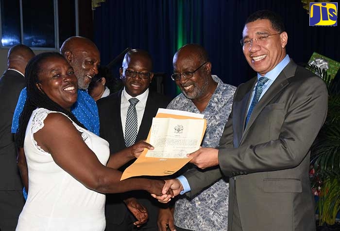 Prime Minister, the Most. Hon. Andrew Holness (right), presents  a certificate of title  to new home owner, Medlyn Dixon (left), during a ceremony at the Greater Portmore Open Bible Church, on Wednesday (December 18). She was among 30 persons who were provided with titles at the event. Also pictured (from second right) are: Member of Parliament for South St. Catherine, Fitz Jackson; Minister without Portfolio in the Ministry of Economic Growth and Job Creation, Senator the Hon. Pearnel Charles Jr.; and  joint title holder with Ms. Dixon, Michael Cole.
