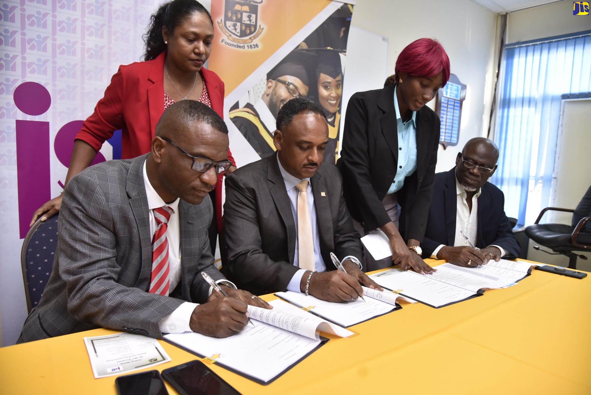 President of The Mico University College, Dr. Asburn Pinnock (left); and Managing Director, Jamaica Social Investment Fund (JSIF), Omar Sweeny (second left), sign a contract for the project, ‘Youth at Risk: Capacity Building for Social Workers and Caregivers in Children’s Homes’, on January 21 at The Mico University College campus in Kingston. Also taking part (at right) is Manager, The Mico Foundation, Burchell Duhaney. Observing (from left, standing) are Project Manager, JSIF, Kemiesha Batchan; and Social Officer, JSIF, Claudia Barrett. The contract, which is valued at $2.6 million, will see the training of Child Protection and Family Services Agency (CPFSA) social workers in administering psycho-social interventions for at-risk youth.