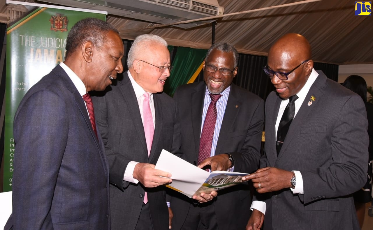 Justice Minister, Hon. Delroy Chuck (second left), peruses a copy of the first ever Strategic Business Plan for the Judicial Arm of Government, during the document