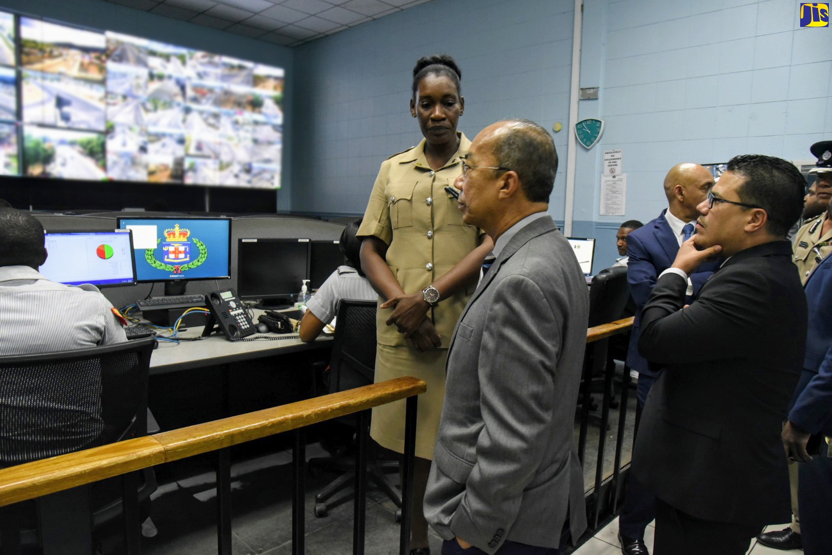 National Security Minister, Hon. Dr. Horace Chang (left, foreground), and Minister without Portfolio in the Ministry, Senator the Hon. Matthew Samuda (right), observe operations inside the Police Emergency Control Centre at the Office of the Police Commissioner in Kingston, during a tour of the facility on Wednesday (March 18). Briefing them is Sub-officer in charge of the Centre, Woman Inspector Vanessa Clarke.