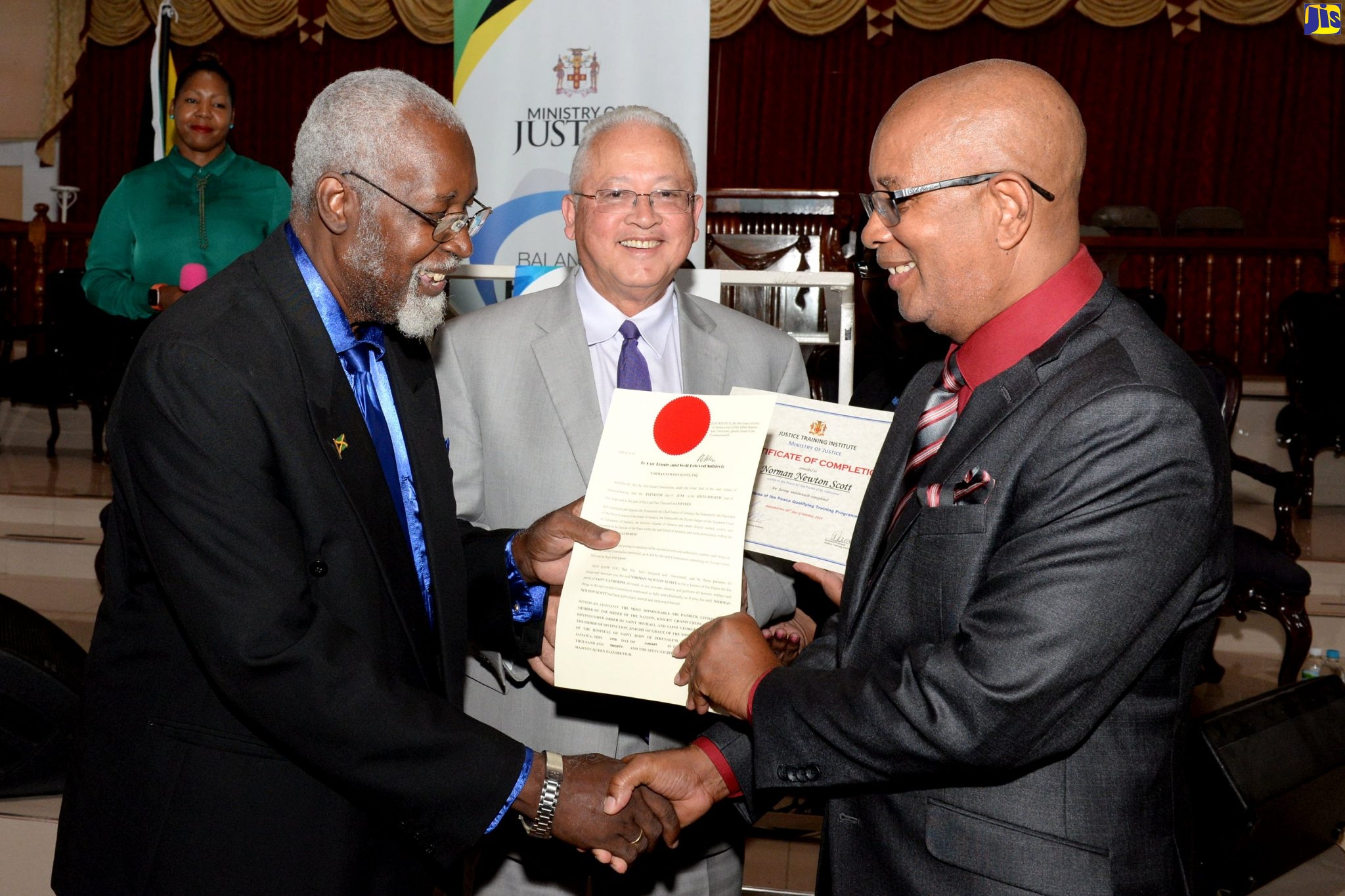 Justice Minister, Hon. Delroy Chuck (centre), observes as Mayor of Spanish Town, Councillor Norman Scott (right), is presented with his certificate and Instrument of Office after being installed as a Justice of the Peace for St. Catherine by Custos Rotulorum for the parish, Hon. Rev. Jeffrey McKenzie. The commissioning ceremony for the 126 new JPs was held at the Portmore Seventh-Day Adventist Church on March 4.