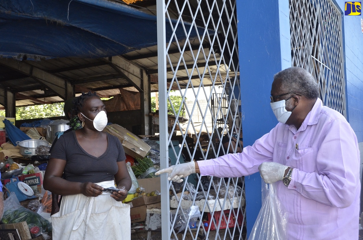 Custos of St. James, Bishop the Hon. Conrad Pitkin (right), informs market vendor, Sabrina Simms (left), about the proper use of the reusable face mask he gave her, when he distributed some 450 washable face masks to vendors and customers at the Charles Gordon Market, in Montego Bay, on Friday (April 24).
