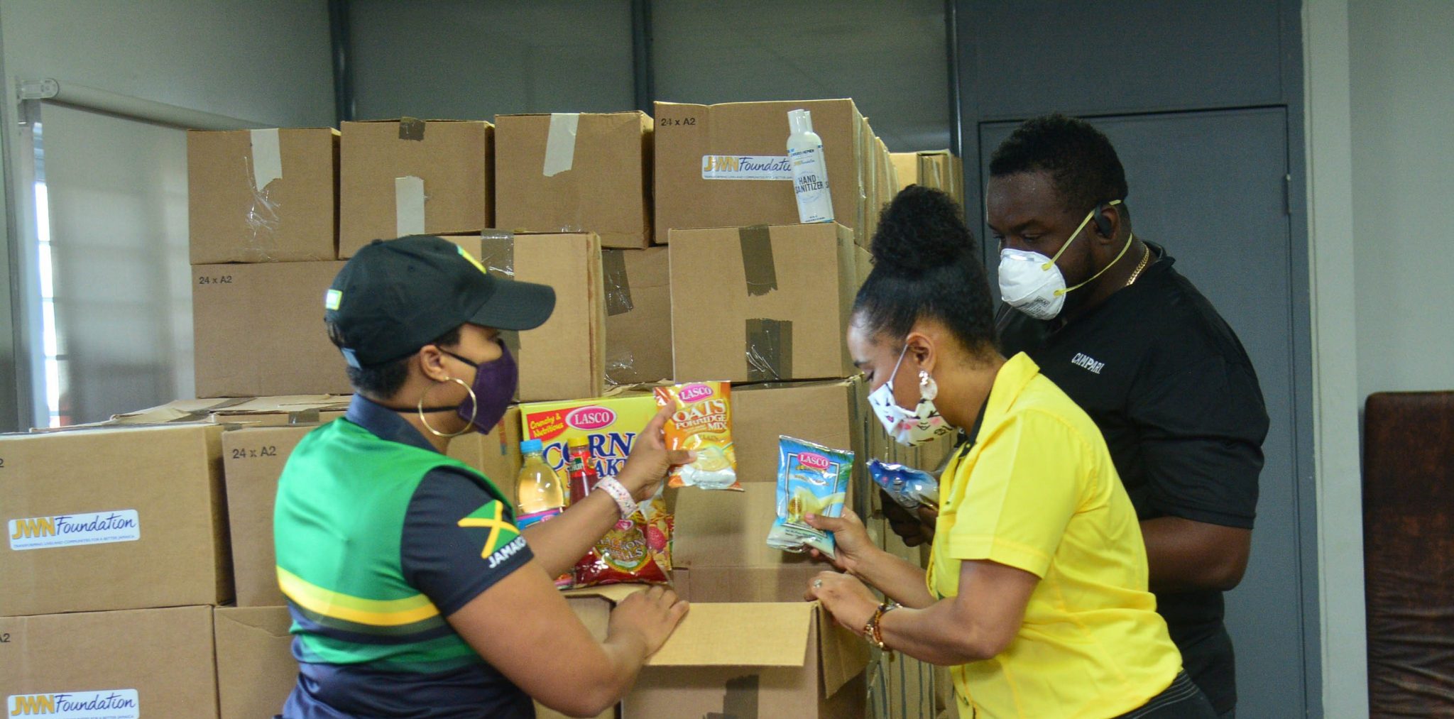 J. Wray and Nephew's Channel and Customer Marketing Director, Lelekia-Dee Barnes (left);  Commercial Director of Jamaica and the Caribbean, Michelle Brown-Sinclair (centre),  and Demand Specialist, Shawn Davidson,  packaging food items to be distributed in communities across Jamaica in response to the COVID-19 pandemic. 

