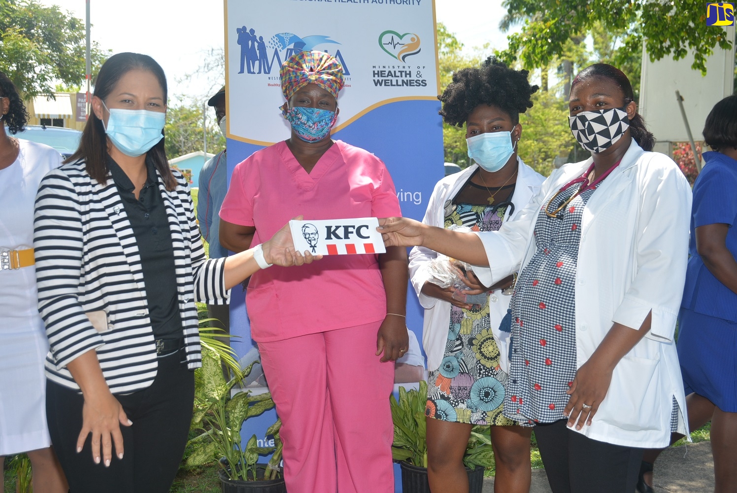 Marketing Director of Restaurants of Jamaica (ROJ), Tina Myers-Matalon (left), making a symbolic presentation to member of the Jamaica Medical Doctors Association (JMDA), Cornwall Regional Hospital, Tionette Allen (right), for the 500 KFC treats to frontline workers at the Type A institution in St. James, during a ceremony on Wednesday, May 13. In the background are (from left): Registered Nurses, Simone Crawford-Headley and Crena Henry.