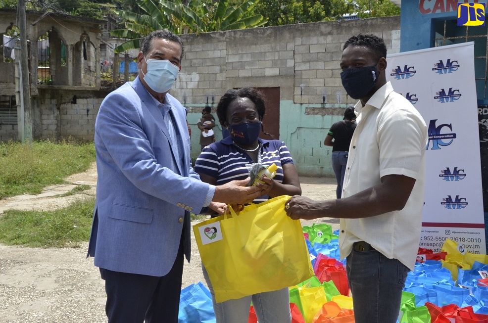 Mayor of Montego Bay, Councillor Homer Davis (left), presents a bag of groceries to Marjorie Mitchell (centre) on Tuesday (July 21), during a food distribution drive in Canterbury, Montego Bay, St. James under the first phase of the Coronavirus (COVID-19) Response Programme sponsored by UN-HABITAT and the St. James Municipal Corporation.  Sharing the moment is Councillor for the Montego Bay South Division, Richard Vernon.