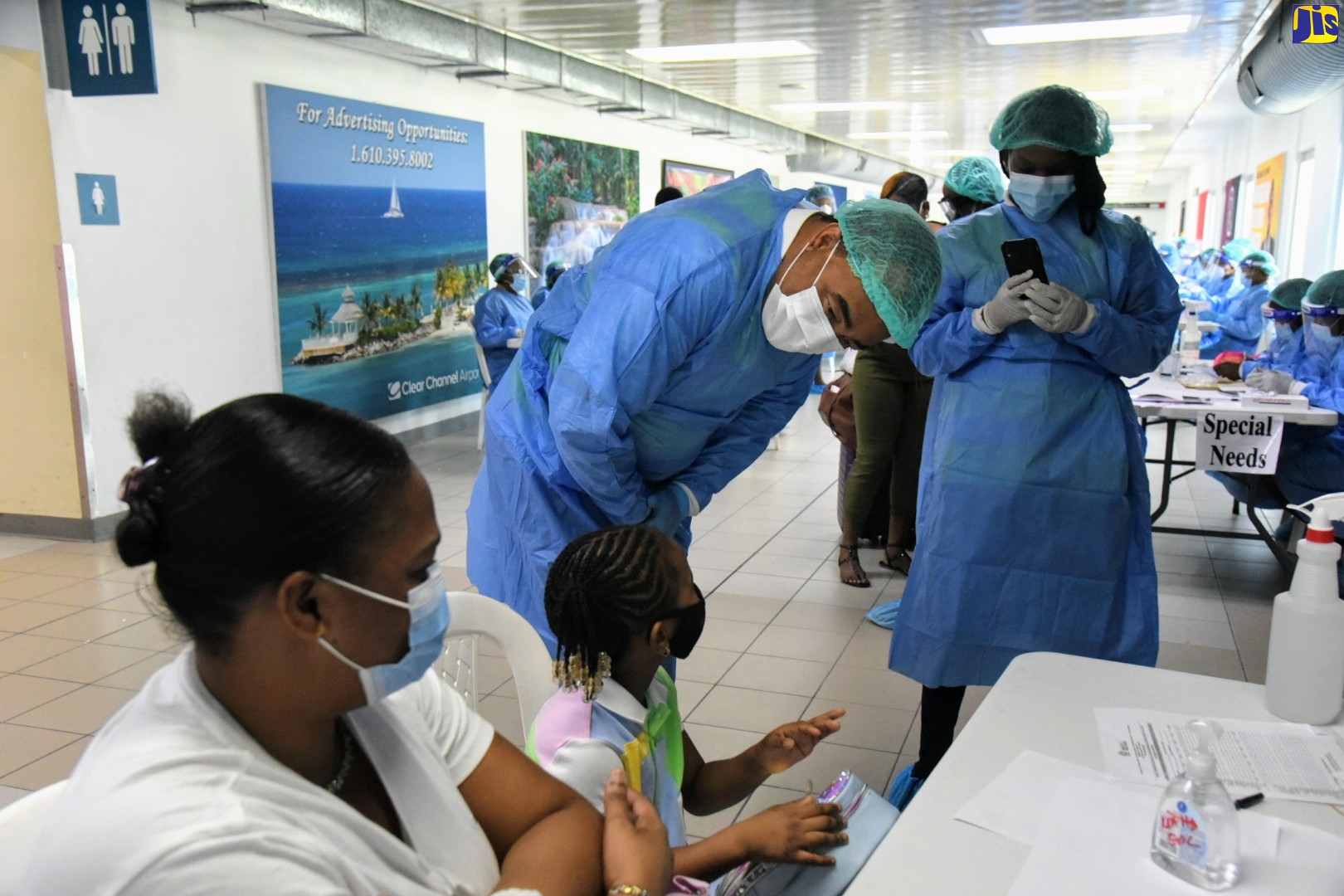Minister of Health and Wellness, Dr. the Hon. Christopher Tufton (second right), engages with a little girl while she and her mother were being processed at the Norman Manley International Airport in June 9. They were among several Jamaicans, who arrived on a flight from Fort Lauderdale in the United States under the protocol for controlled re-entry.