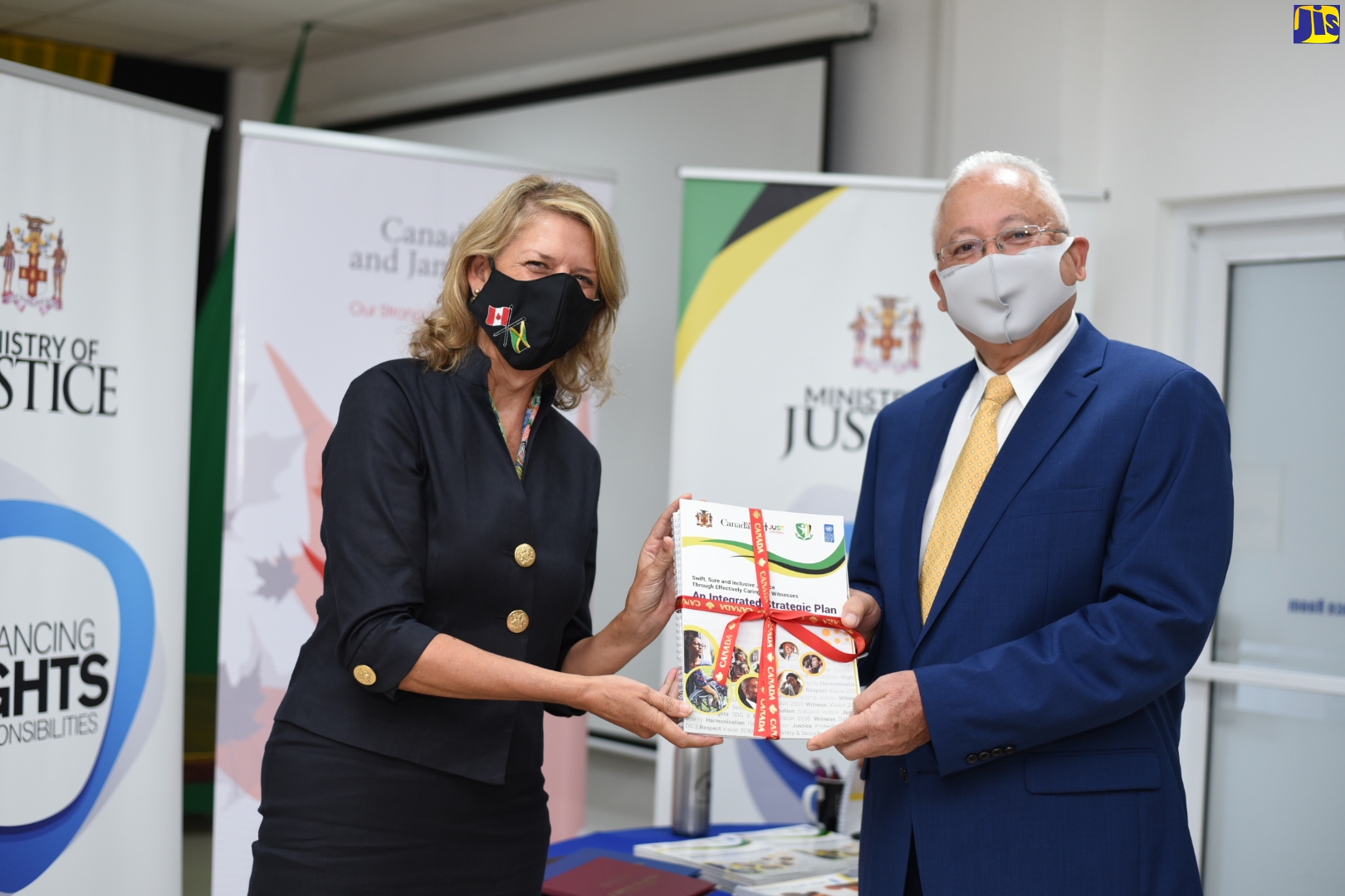 Canadian High Commissioner to Jamaica, Her Excellency Laurie Peters (left) hands over a copy of the Witness Care Strategy and Action Plan to Minister of Justice, Hon. Delroy Chuck, at the Ministry