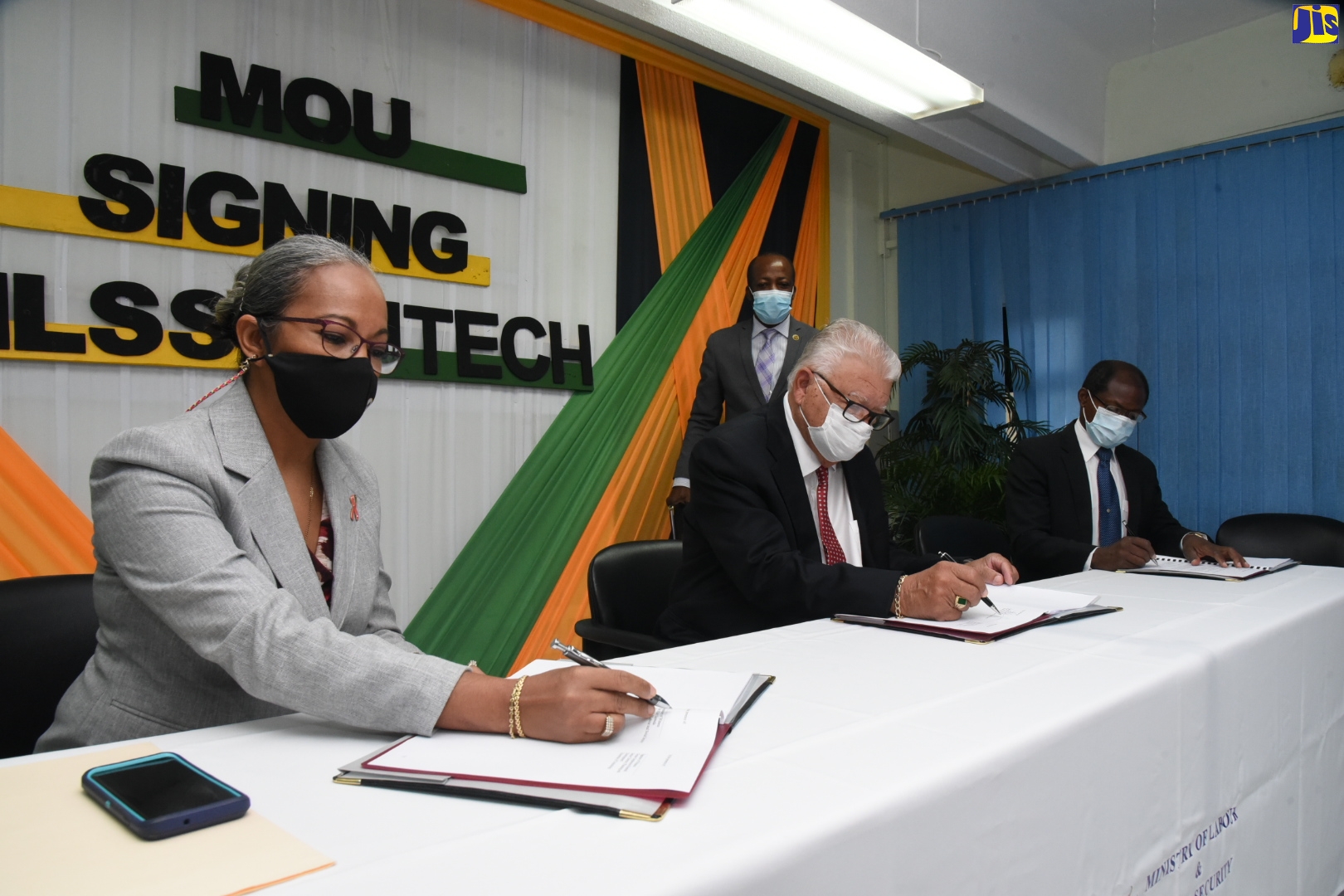 Labour and Social Security Minister, Hon. Karl Samuda (second left), signs a Memorandum of Understanding (MoU) to establish partnership with the University of Technology (UTech) to promote the Labour Market Information System (LMIS) during a ceremony held at the Ministry’s North Street address in Kingston on Friday (October 23). Also signing (from left) are Permanent Secretary in the Ministry, Colette Roberts Risden; and Acting President of the University of Technology (UTech), Professor Colin Gyles. Looking on in the background is Director, Public Relations and Communications in the Ministry, Vando Palmer.