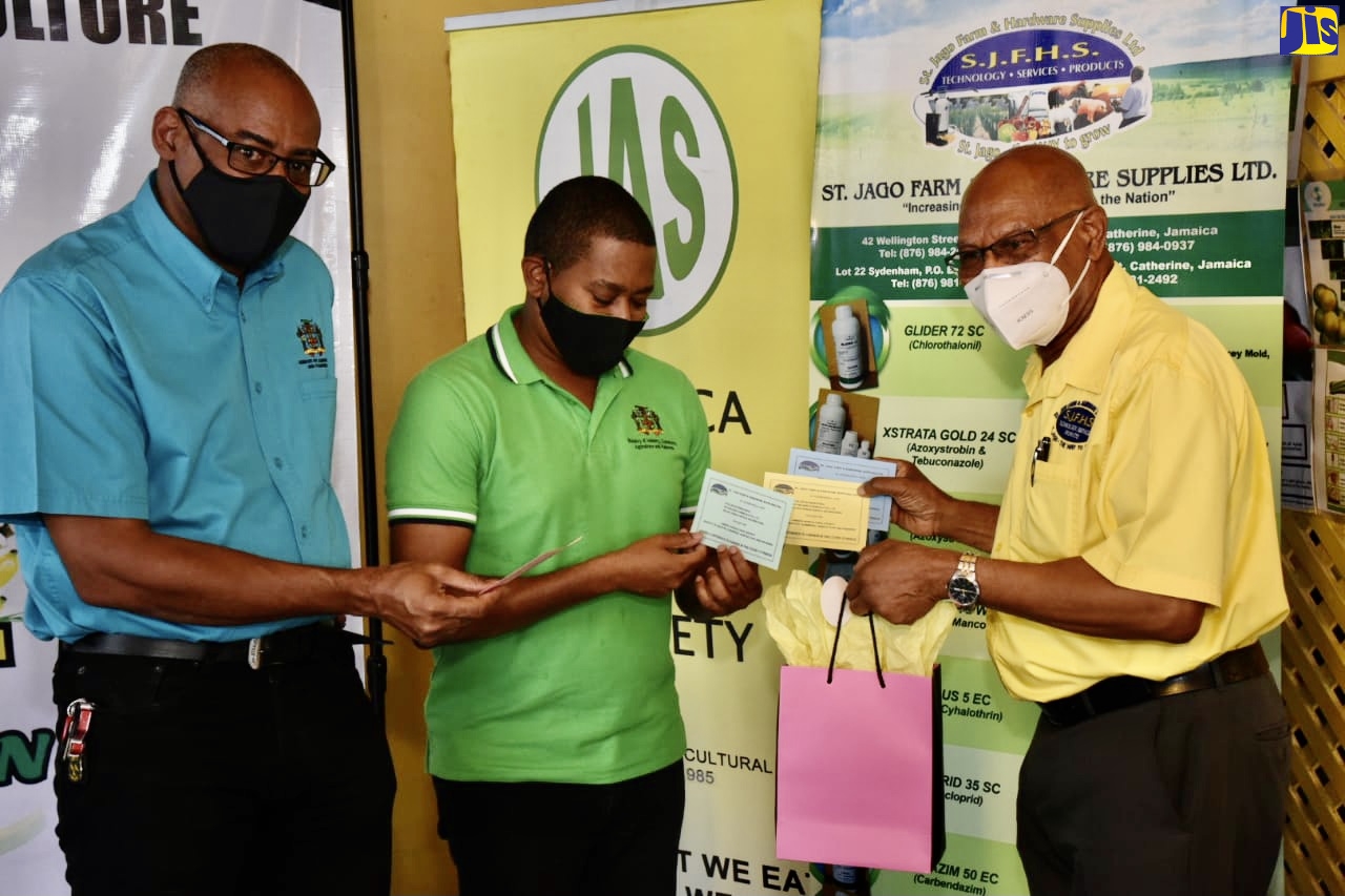 Minister of Agriculture and Fisheries, Hon. Floyd Green (centre), looks at one of the vouchers that St. Jago Farm and Hardware Supplies Limited is making available to farmers who have been impacted by the coronavirus (COVID-19) pandemic. Managing Director of the company, O