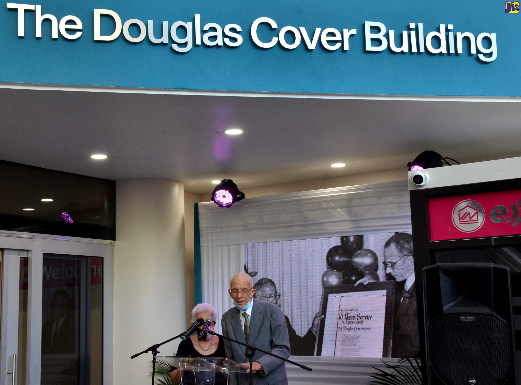 Former General Manager, Victoria Mutual Building Society (VMBS), Douglas Cover, addresses ceremony for the naming of the Victoria Mutual Chief Office and Duke Street Building in his honour as ‘The Douglas Cover Building’ during a ceremony today (November 12). Mr. Cover is being assisted by his wife, Judith. Mr. Cover was recognised for his exemplary commitment to the Victoria Mutual Group and for being an outstanding champion for financial inclusion.
