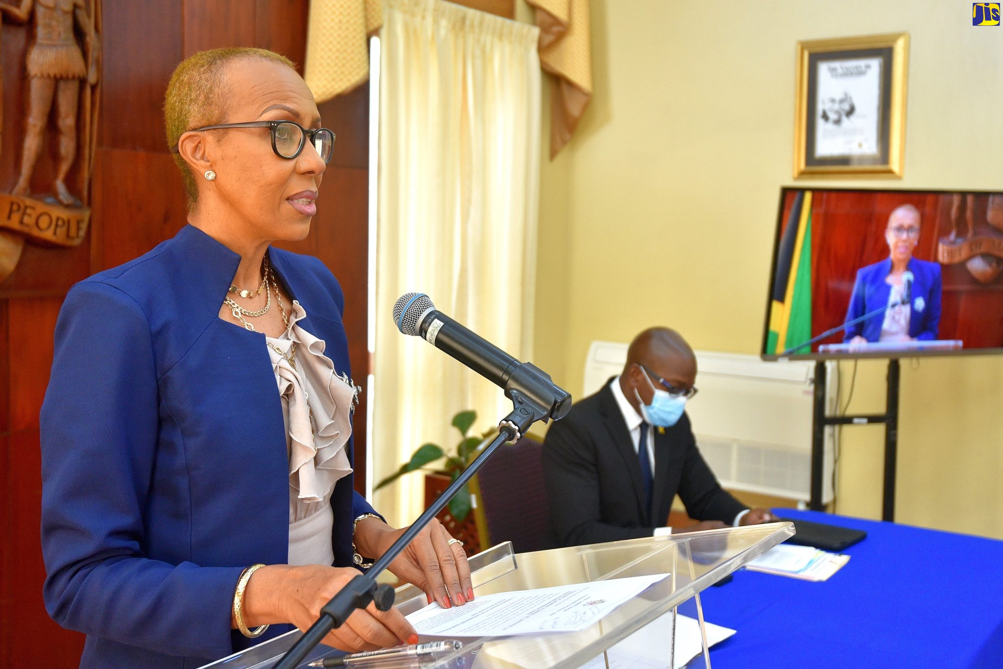 Minister of Education, Youth and Information, Hon. Fayval Williams (at lectern), addresses a virtual post-Cabinet press briefing on Wednesday (December 9) from Jamaica House. Seated is Minister of Housing, Urban Renewal, Environment and Climate Change, Hon. Pearnel Charles Jr.  

