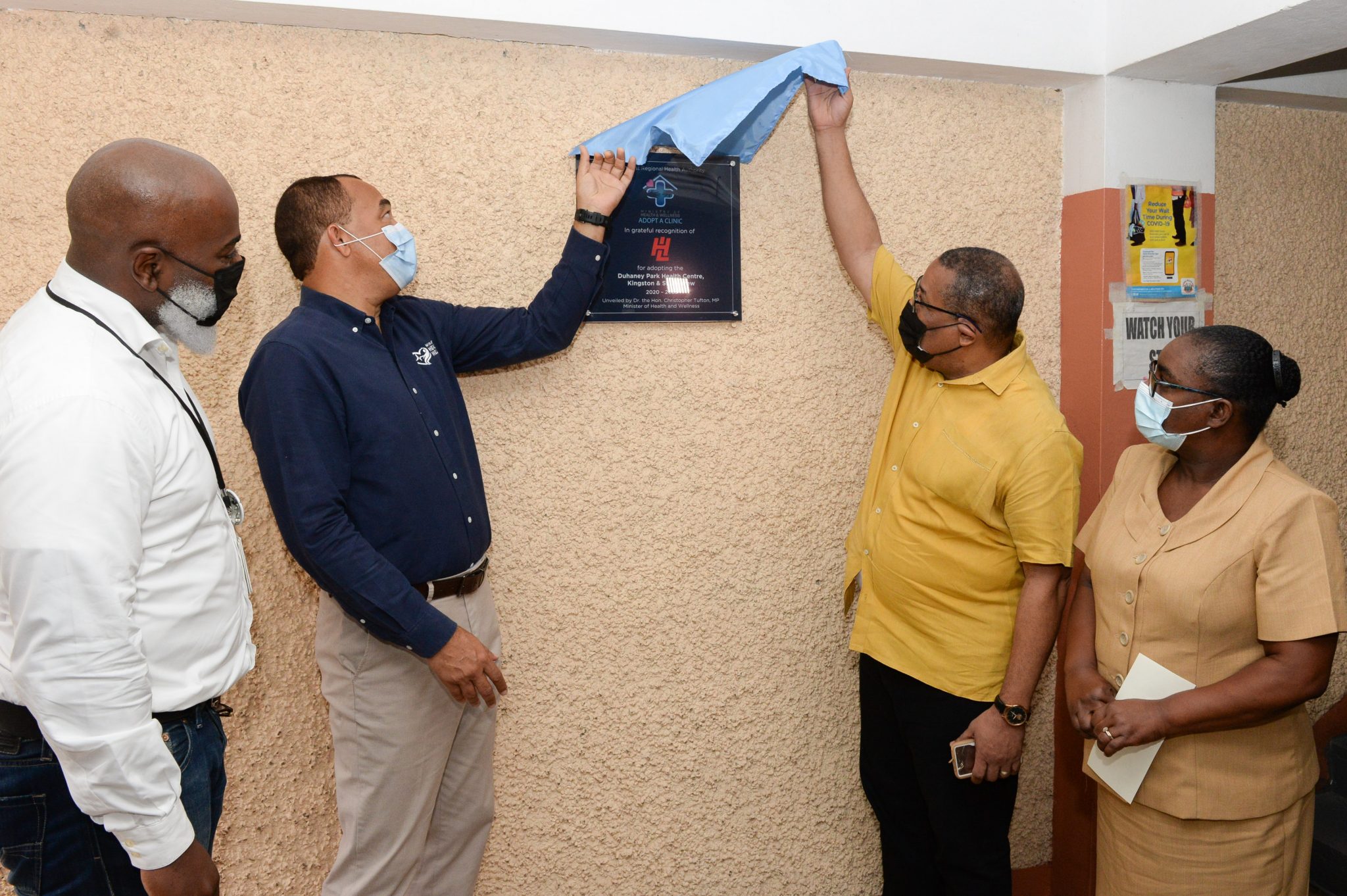Health and Wellness Minister, Dr. the Hon. Christopher Tufton (second left) and Member of Parliament, St. Andrew Western, Anthony Hylton (third left),  unveil a plaque during the ceremony for the formal adoption of the Duhaney Park Health Centre by Hardware and Lumber, under the Ministry of Health and Wellness