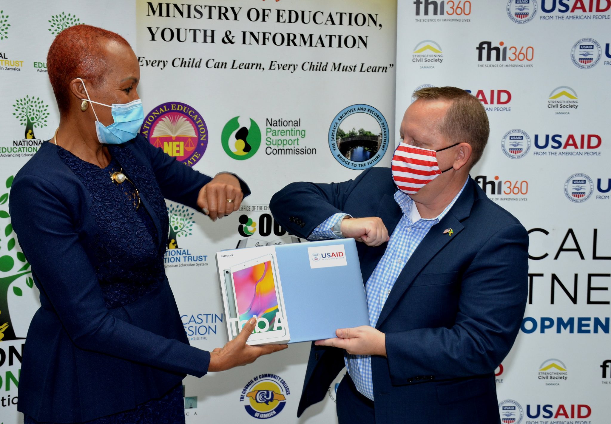 Minister of Education, Youth and Information,  Hon. Fayval Williams (left), knocks elbows with Charge d’Affaires, United States Embassy in Jamaica, John McIntyre, on Tuesday (February 2), at the Ministry, at Heroes Circle, in Kingston, after accepting samples of computers to be distributed among 10 schools.

