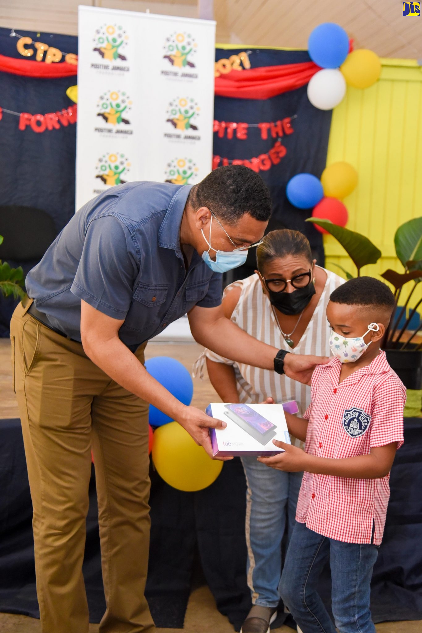 Prime Minister, the Most Hon. Andrew Holness (left), presents student of Clark’s Town Primary School in Trelawny, Aiden Blake, with a tablet computer, during a ceremony at the school on Friday (July 2). Sharing in the occasion is Member of Parliament for Trelawny Southern, Marissa Dalrymple Philibert. The Prime Minister donated 40 tablets to students from seven primary-level schools in Southern Trelawny, through his Positive Jamaica Foundation.