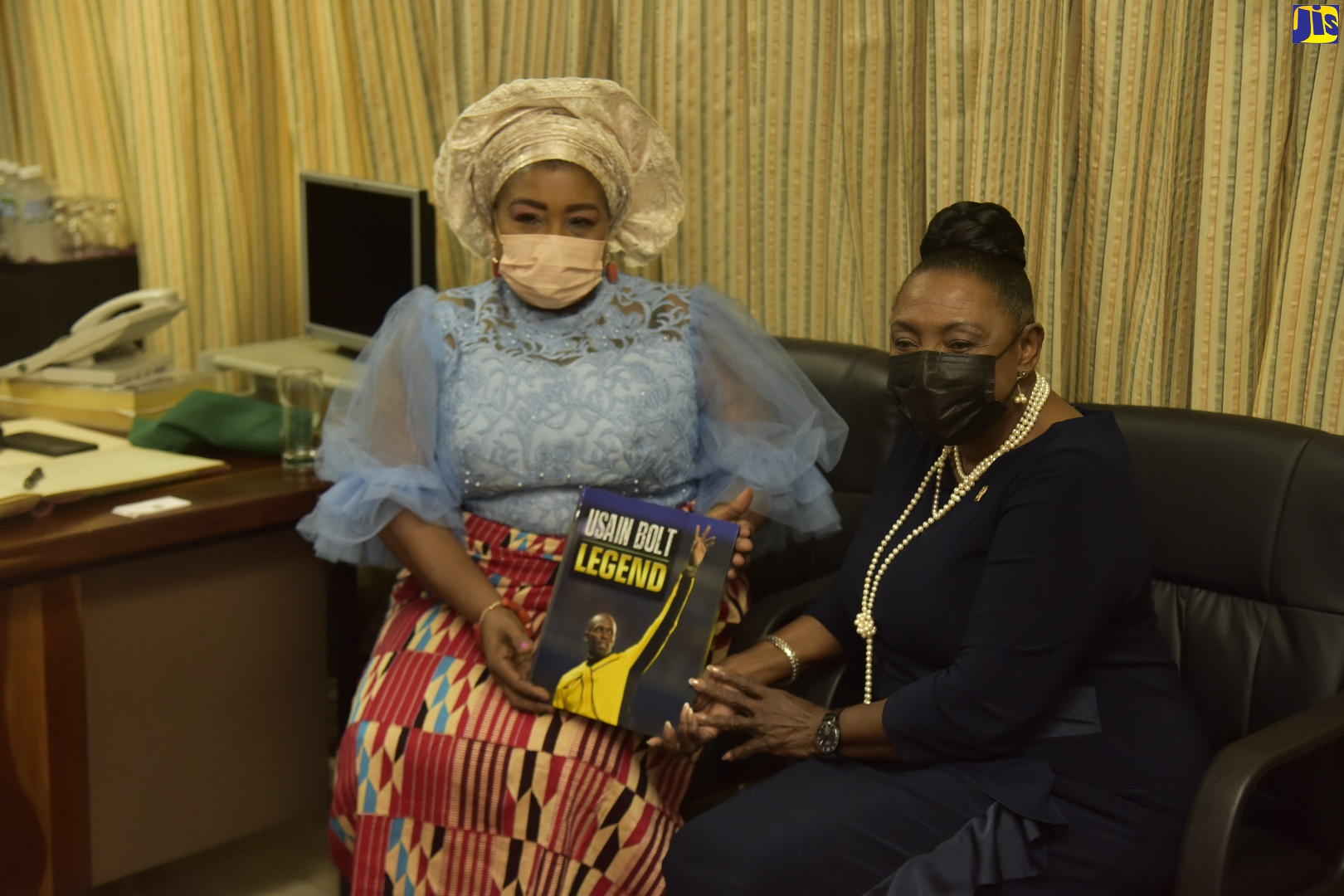 Minister of Culture, Gender, Entertainment and Sport, Hon. Olivia Grange (right), presents High Commissioner for the Republic of Nigeria to Jamaica, Her Excellency Dr. Maureen Tamuno, with a copy of the book entitled ‘Usain Bolt Legend’ during a courtesy call at Gordon House on July 20.
