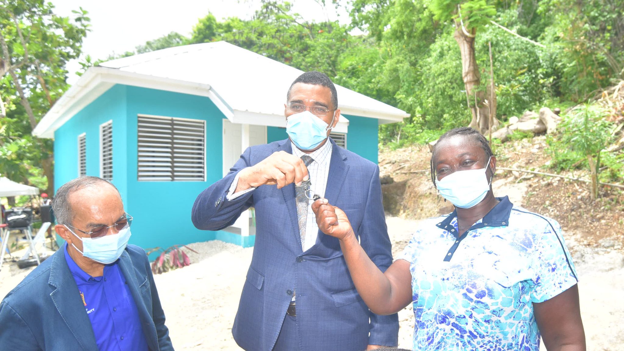 Prime Minister, the Most Hon. Andrew Holness, hands over the keys to a new three-bedroom house built under the Government's new Social Housing Programme to resident Marva Mason (right), during a ceremony in Quarry, St. James, on Wednesday (July 14). Looking on is Deputy Prime Minister & Minister of National Security, Hon. Dr. Horace Chang.    Yhomo Hutchinson Photos


