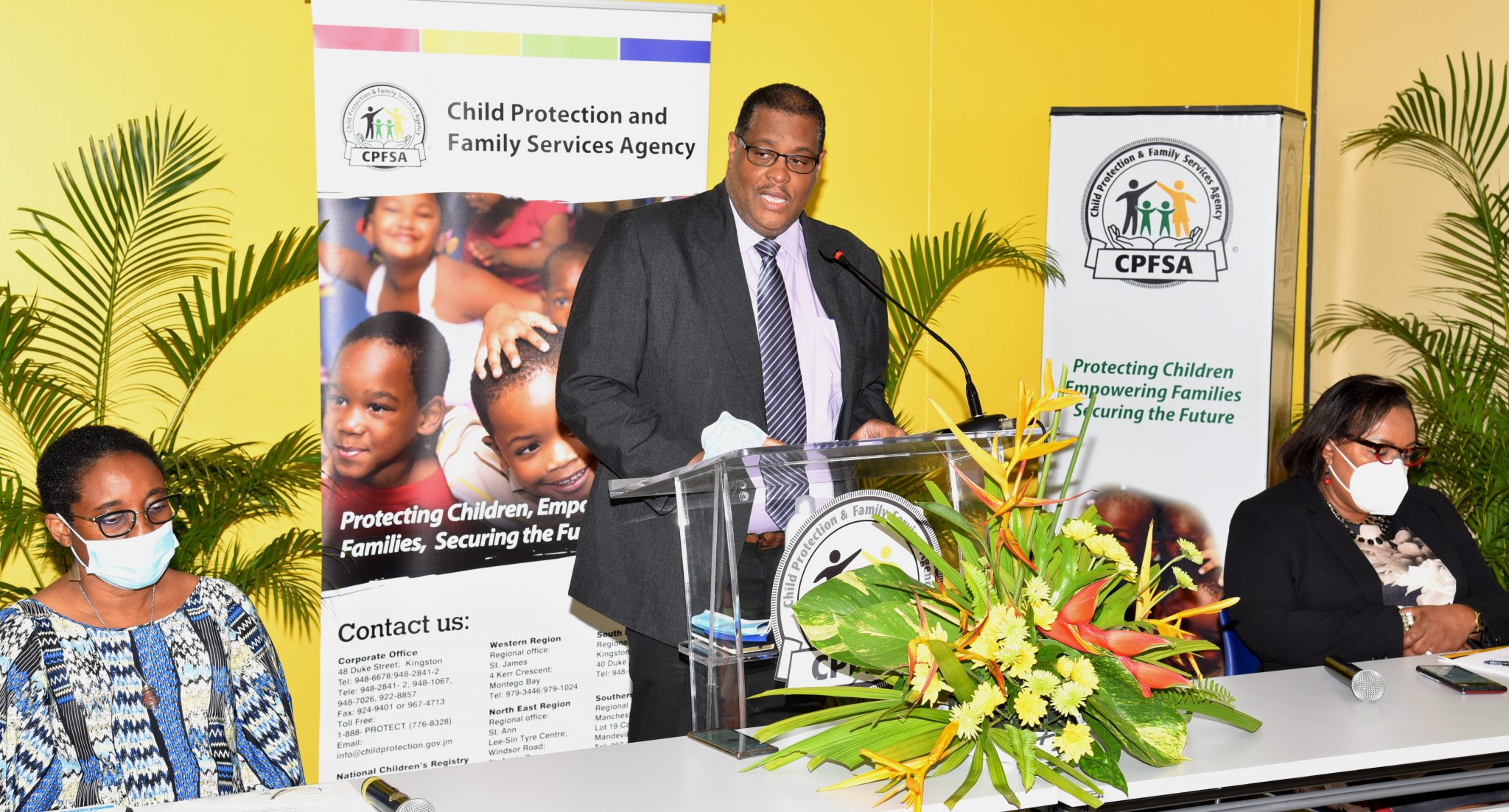 Director of Policy, Planning and Evaluation in the Child Protection and Family Services Agency (CPFSA), Newton Douglas (at podium),  addresses the CPFSA’s virtual quarterly press briefing on Wednesday (July 14), which was broadcast from the downtown Kingston offices of the agency. Listening  (from left) are Principal Director, Institute for Applied Social Research (IASR), Dr. Joy Brown; and Chief Executive Officer of the CPFSA, Rosalee Gage-Grey.

