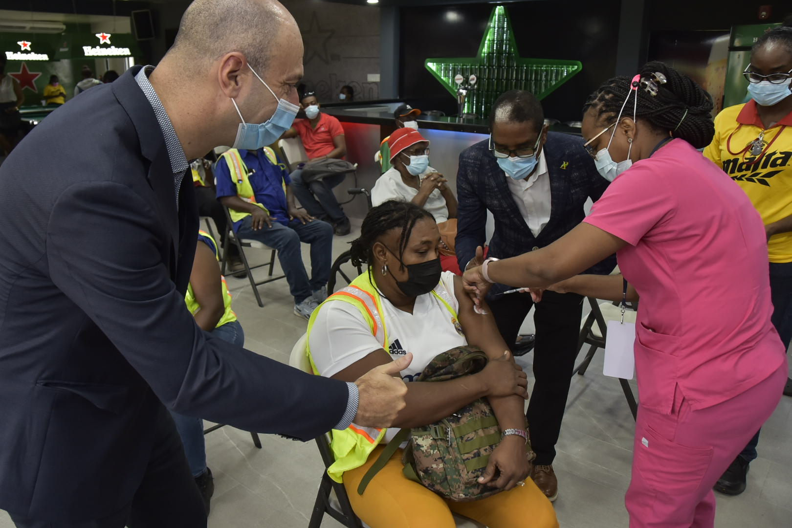 Minister of State for the Ministry of Industry, Investment and Commerce, Hon. Dr. Norman Dunn, (second right), observing Nurse Shannon Bowden (right), as she administers the vaccine to a Red Stripe employee (centre). Red Stripe’s Managing Director, Luis Prata, cheered his employee, as she received her dose. The vaccination was administered at the company’s brewery on Spanish Town Road in Kingston today (September 8).