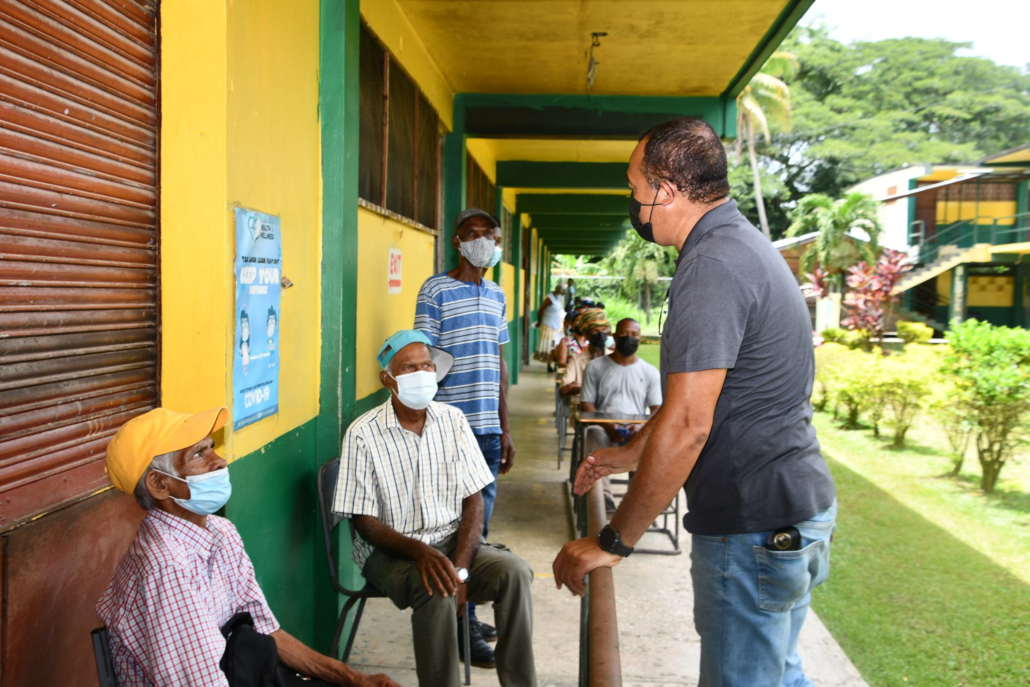Minister of Health and Wellness, Dr. the Hon. Christopher Tufton (right), talks with citizens awaiting vaccination at the Grange Hill High School in Westmoreland on Thursday ( September 2). He was visiting vaccination sites and engaging in community sensitisation sessions in the parish.

