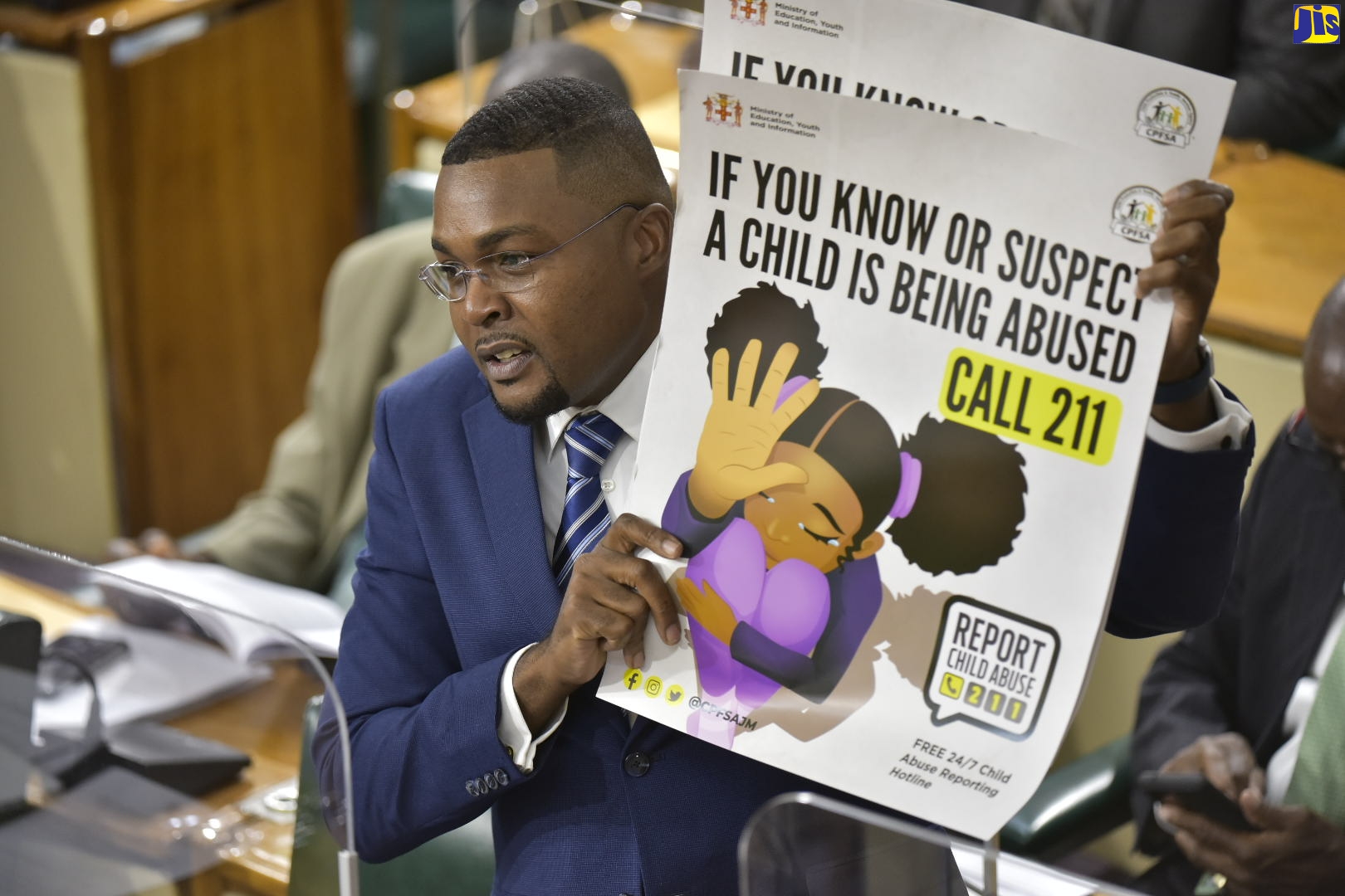 State Minister in the Ministry of Education, Youth and Information, Hon. Robert Morgan, shows a poster providing information about the 211 child abuse reporting hotline, which he requested Members of Parliament (MPs) to place in their constituency offices to aid in the fight against child abuse. The poster forms part of the information package on the hotline Mr. Morgan has put together for distribution by MPs to their constituents. Mr. Morgan was making his contribution to the 2021/22 State of the Constituency Debate during the sitting of the House of Representatives on Tuesday (October 12).