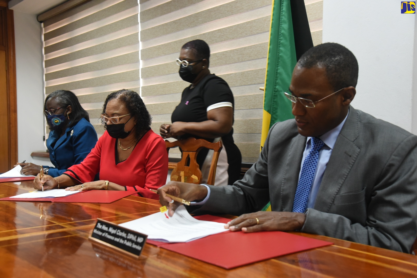 Minister of Finance and the Public Service, Dr. the Hon Nigel Clarke (right), and (from left, seated) Financial Secretary in the Finance Ministry, Darlene Morrison, and Jamaica Confederation of Trade Unions (JCTU) President, Helene Davis Whyte, sign the 2021/22 Heads of Agreement for wage increases for public sector workers represented by JCTU member unions. The signing was held at the Ministry in Kingston, on Friday (October 29). Overseeing the proceedings is the Ministry’s Principal Director for Employee Relations, Lorna Phillips.