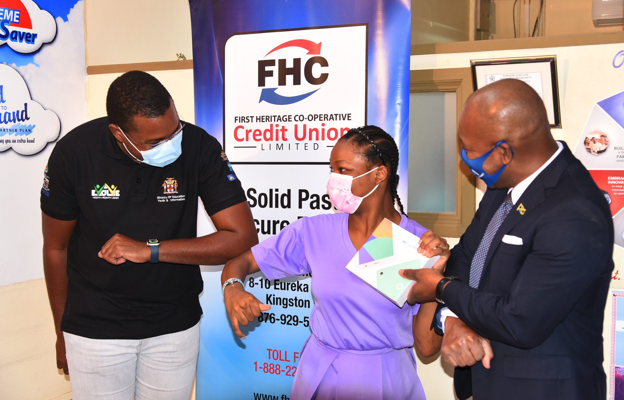 State Minister for Education, Youth and Information, Hon. Robert Morgan (left), greets Jaden Lois Barker (centre) of the Lister Mair Gilby High School for the Deaf-May Pen Unit, as she receives a tablet from Branch Manager, First Heritage Co-operative (FHC) Credit Union Limited May Pen, Norman Williams. Mr. Morgan was participating in the handover of eight tablets to students of the Clarendon-based institution by FHC Credit Union Limited, at the entity’s May Pen Branch office on Monday (December 13).