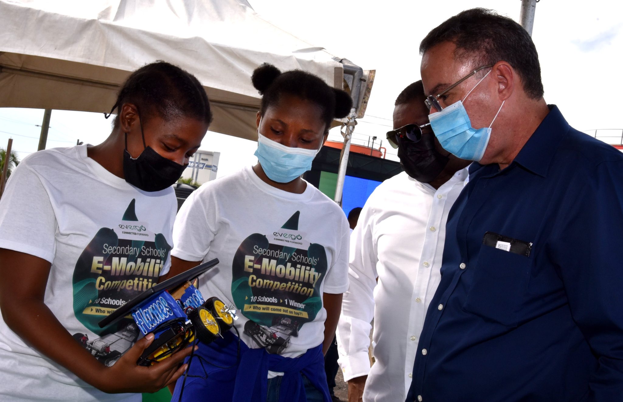 Minister of Science, Energy and Technology, Hon. Daryl Vaz (right); and President and Chief Executive Officer (CEO) of Evergo Jamaica, Wayne McKenzie (second right) look on as students of Immaculate Conception High School (from left) Courtney-Kay White; and Nikaela Carthy, demonstrate how a robot they built works. Immaculate Conception was among nine schools that participated in Evergo Jamaica's Secondary Schools Electric Mobility (E-Mobility) Robotics Competition held recently, at the company's Marcus Garvey Drive location in Kingston. Teams showcased how best they could integrate solar energy and batteries to propel wheels by way of a motor.


