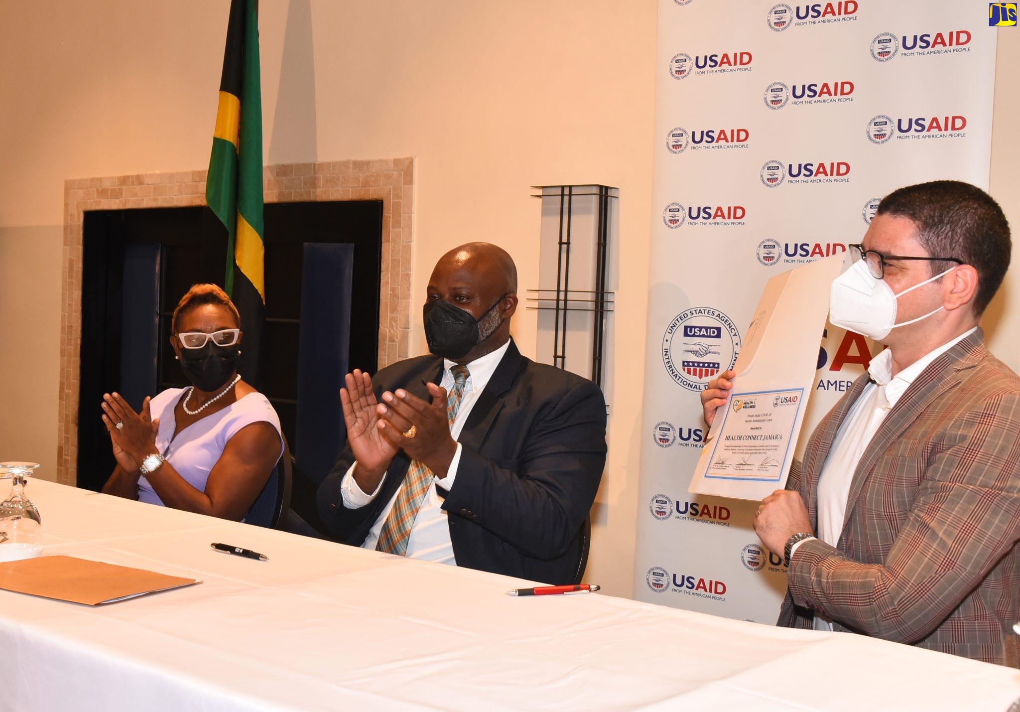 State Minister in the Ministry of Health and Wellness Hon. Juliet Cuthbert Flynn (left), and United States Agency for International Development (USAID)/ Jamaica Country Representative, Jason Fraser (second left) applaud, as Director/Principal Investigator, Health Connect Jamaica Dr Geoffrey Barrow, displays the grant funding certificate the organisation was awarded as one of nine participants in the Private Sector COVID-19 Vaccine Administration Partnership. Under this arrangement, private sector entities have been provided with grants by USAID totalling US$600,000 to partner with the government to administer coronavirus (COVID-19) vaccinations to Jamaicans. The presentation was made during the partnership launch at the Jamaica Pegasus Hotel in New Kingston on Friday (Feb. 25).