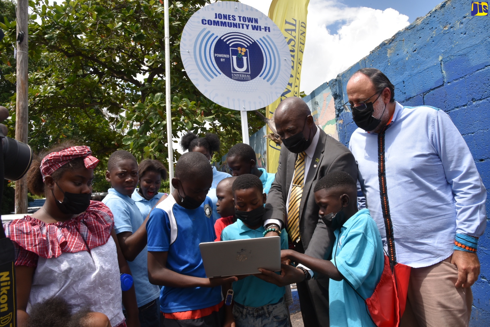 Chief Executive Officer, Universal Service Fund (USF), Daniel Dawes (second right) assists children in accessing the Internet on a laptop, during the commissioning of the community Wi-Fi hotspot at the Jones Town Primary School in St. Andrew, recently. Looking on is Member of Parliament for South St. Andrew and Leader of Opposition, Mark Golding.