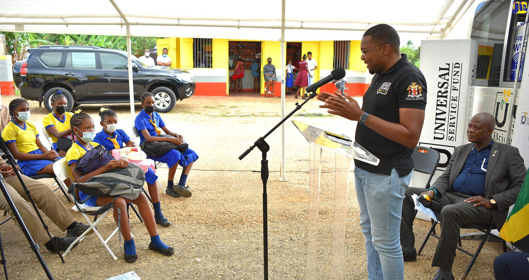 Minister without Portfolio in the Office of the Prime Minister, and Member of Parliament for Clarendon North Central, Hon. Robert Morgan (at lectern), addresses students in attendance at a ceremony to launch a free community Wi-Fi hotspot in Stewarton Square, Mocho, Clarendon, on Thursday (March 10). The hotspot was established in the Stewarton District by the Universal Service Fund (USF) as part of the Government