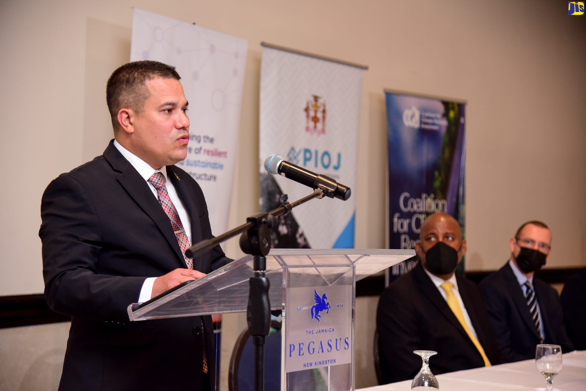 Minister without Portfolio in the Ministry of Economic Growth and Job Creation, Senator the Hon. Matthew Samuda (at lectern), addresses attendees at a ceremony to officially launch the Jamaica Systemic Risk Assessment Tool (J-SRAT) held at The Jamaica Pegasus hotel in New Kingston on Tuesday (May 3). Pictured at the head table (from left) are Director-General of the Planning Institute of Jamaica (PIOJ), Dr. Wayne Henry; and Head, Political and Development Team, British High Commission, Oliver Blake.  