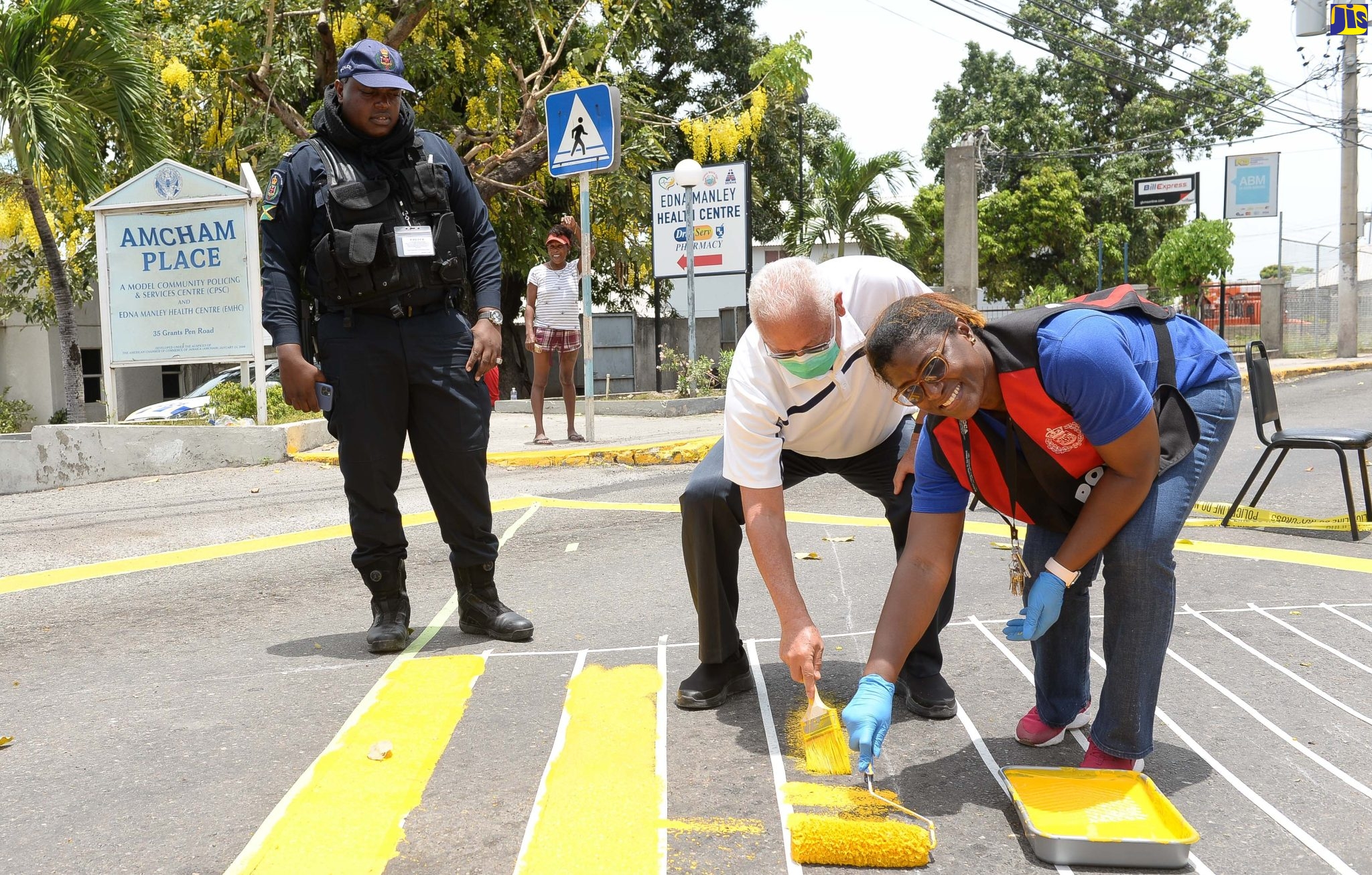 Justice Minister, Hon. Delroy Chuck (centre), and Territorial Officer, St. Andrew North Community Safety and Security Branch, Jamaica Constabulary Force (JCF), Inspector Cheree Greaves (right), paint a grid along a section of Grants Pen Road during Labour Day activities on Monday (May 23). Looking on is Branch member, Constable Corwin Moodie.